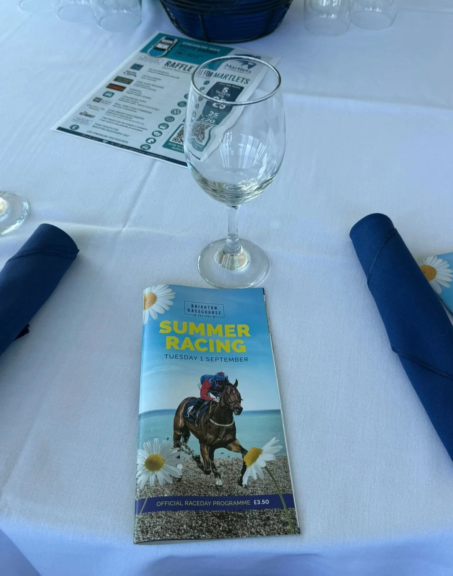 Wine glass and Brighton Racecourse programme beside the Martlets Hospice raffle prize list on a table