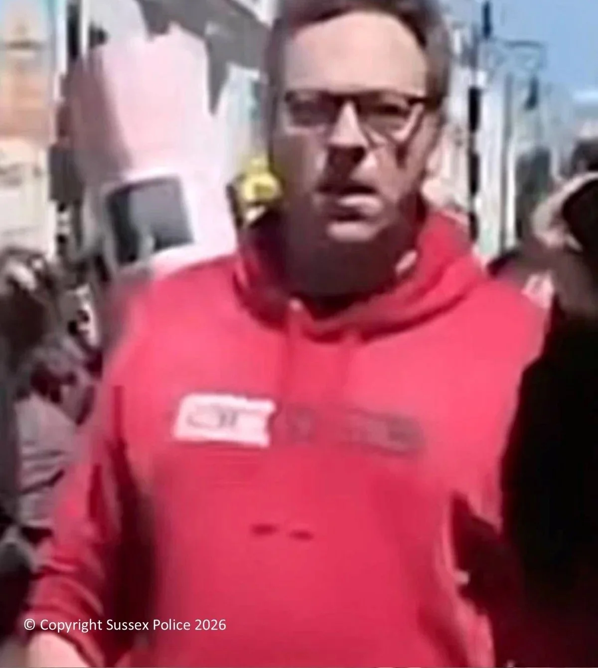 Sussex Police appeal image of a man in a red hoodie and glasses, sought in connection with an alleged assault at a Brighton protest