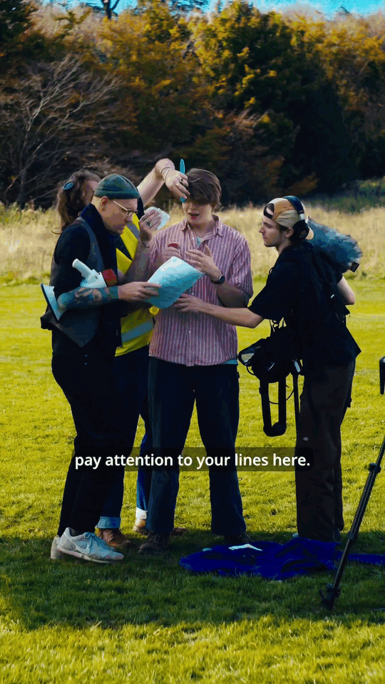 Group of four people gathered outdoors on a grassy field, reviewing documents and equipment, with trees in the background. One person is giving instructions, with a caption saying, "pay attention to your lines here."