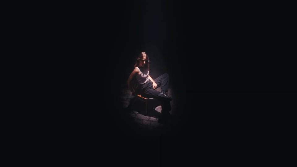 A person sitting on a chair in a dark room with a spotlight on them.