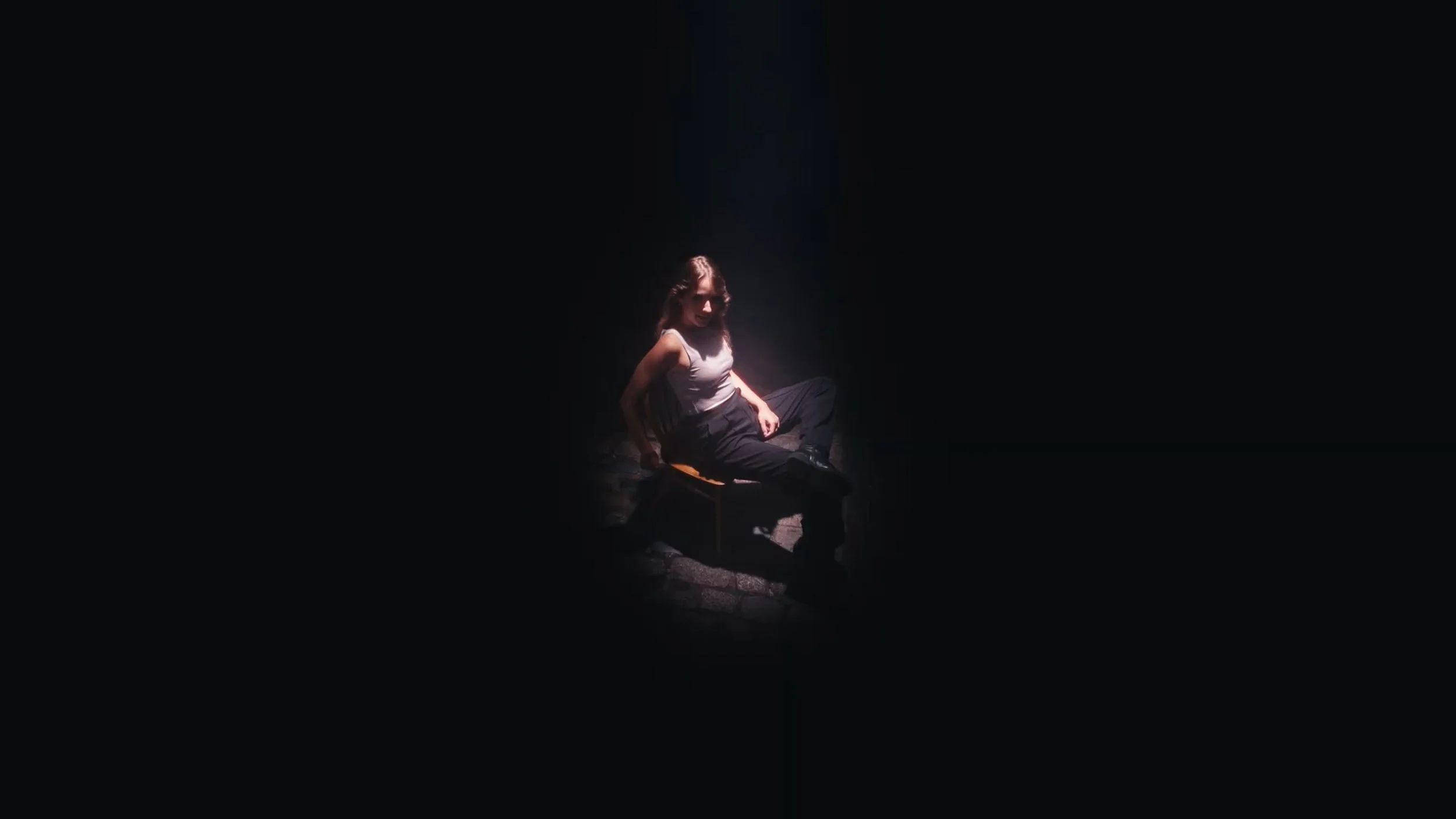 A woman sitting on a chair in a dark room illuminated by a spotlight.