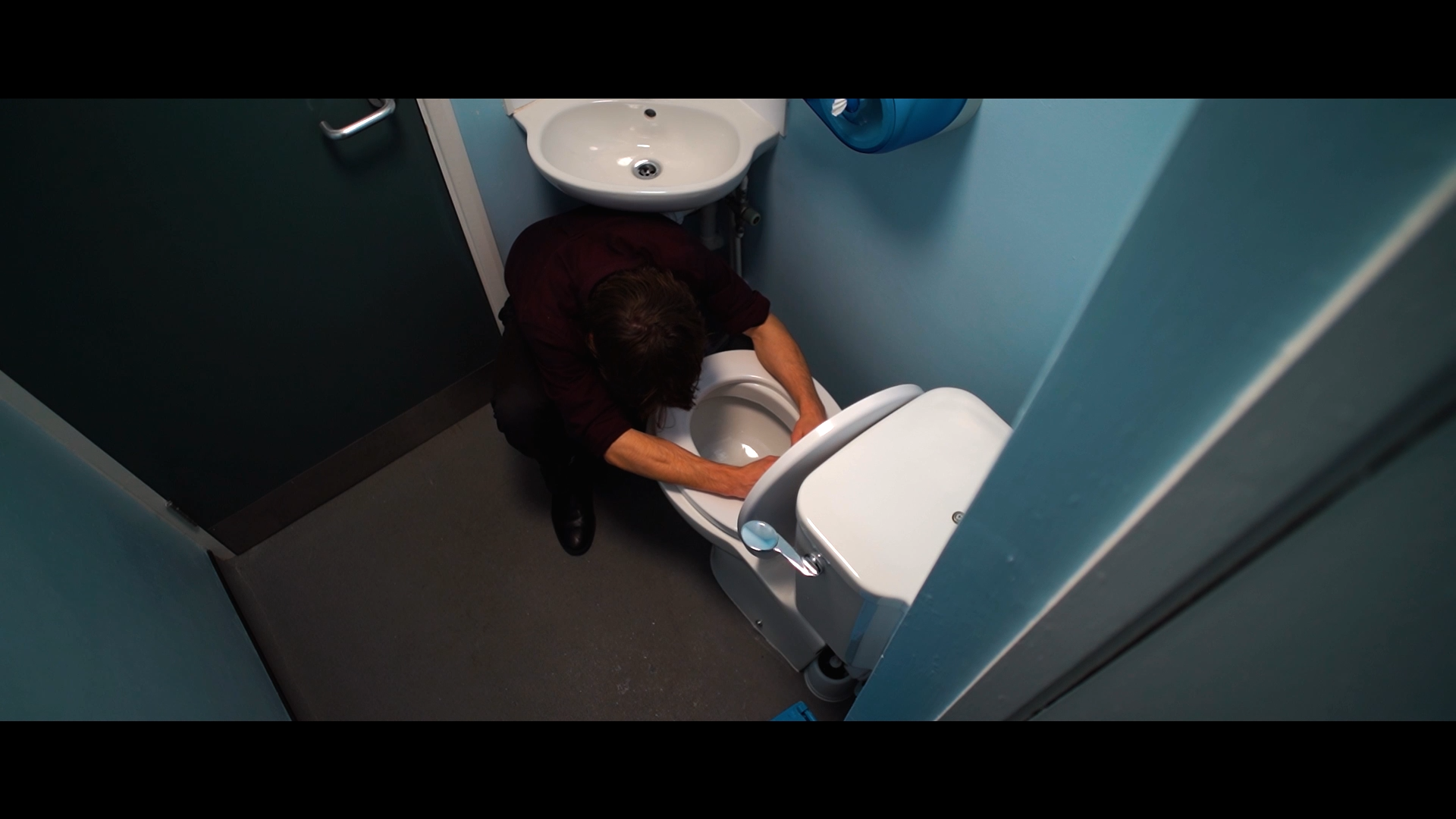 Top view of a man cleaning a toilet in a small bathroom.
