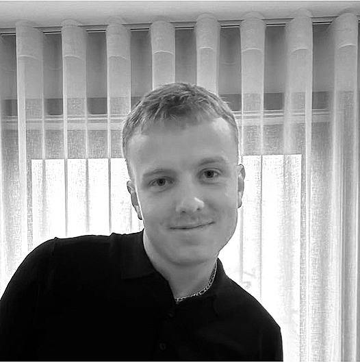 Two young men having a conversation outdoors, with leafless trees in the background.