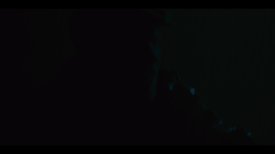 Dark image with barely visible person's face in shadow, possibly in a dimly lit room or environment.