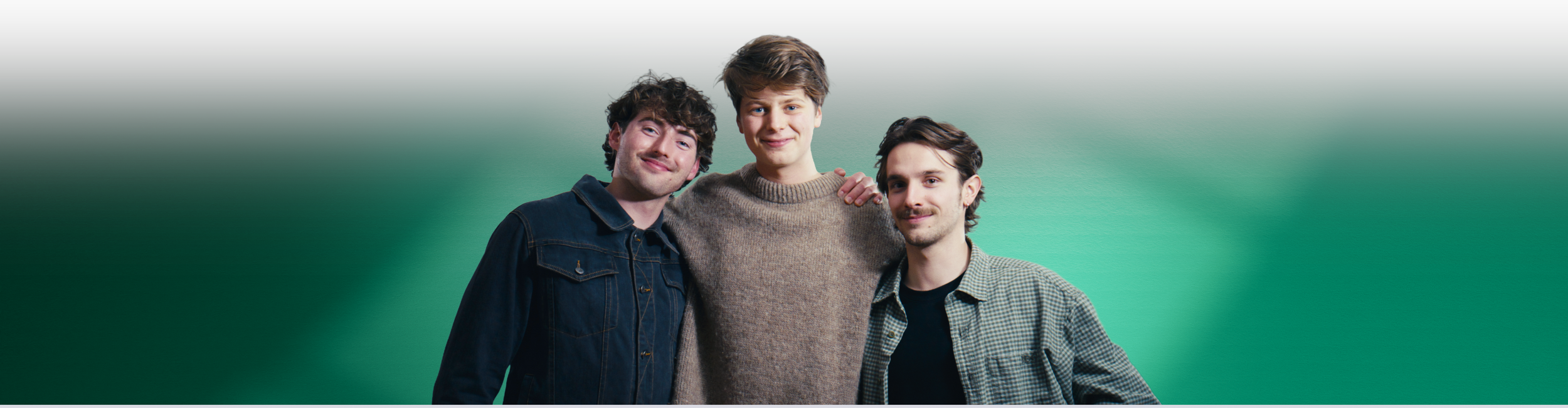 Three young men stand together against a green background, smiling at the camera. These men are the three founders of Mad Heron - Joe Shale, Jasper Pagan and Lewis Kerr.