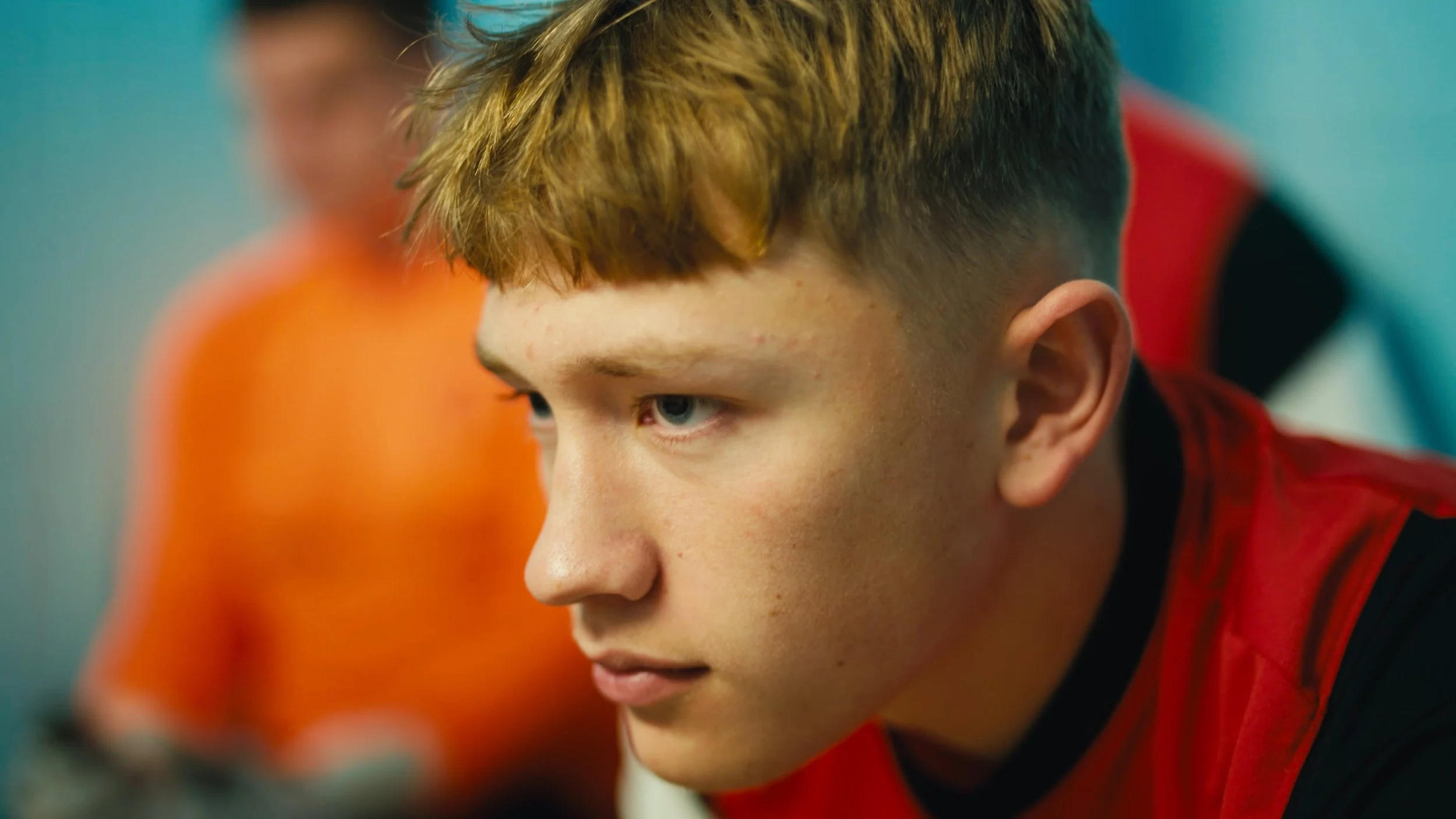 Close-up of a young boy with red hair and blue eyes, wearing a red and black sports uniform, focused on something in front of him.