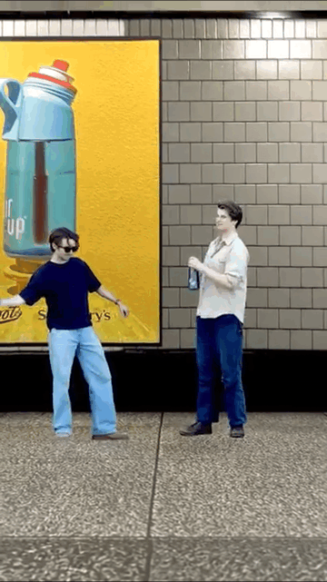 Two people fight over a water bottle in front of a yellow advertisement for AirUp in a London Tube station.