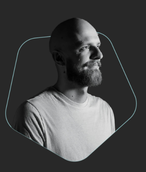 Two men discussing a camera in a workspace, one with a baseball cap, both wearing black T-shirts, in a black-and-white photo.