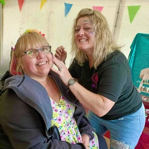 Helen Wilson applying glitter to a woman's face at Womanifest.