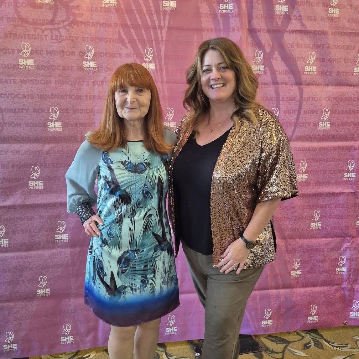 Sue France and Helen Wilson standing in front of a pink backdrop with 'SHE Inspires' logos, smiling for the camera.
