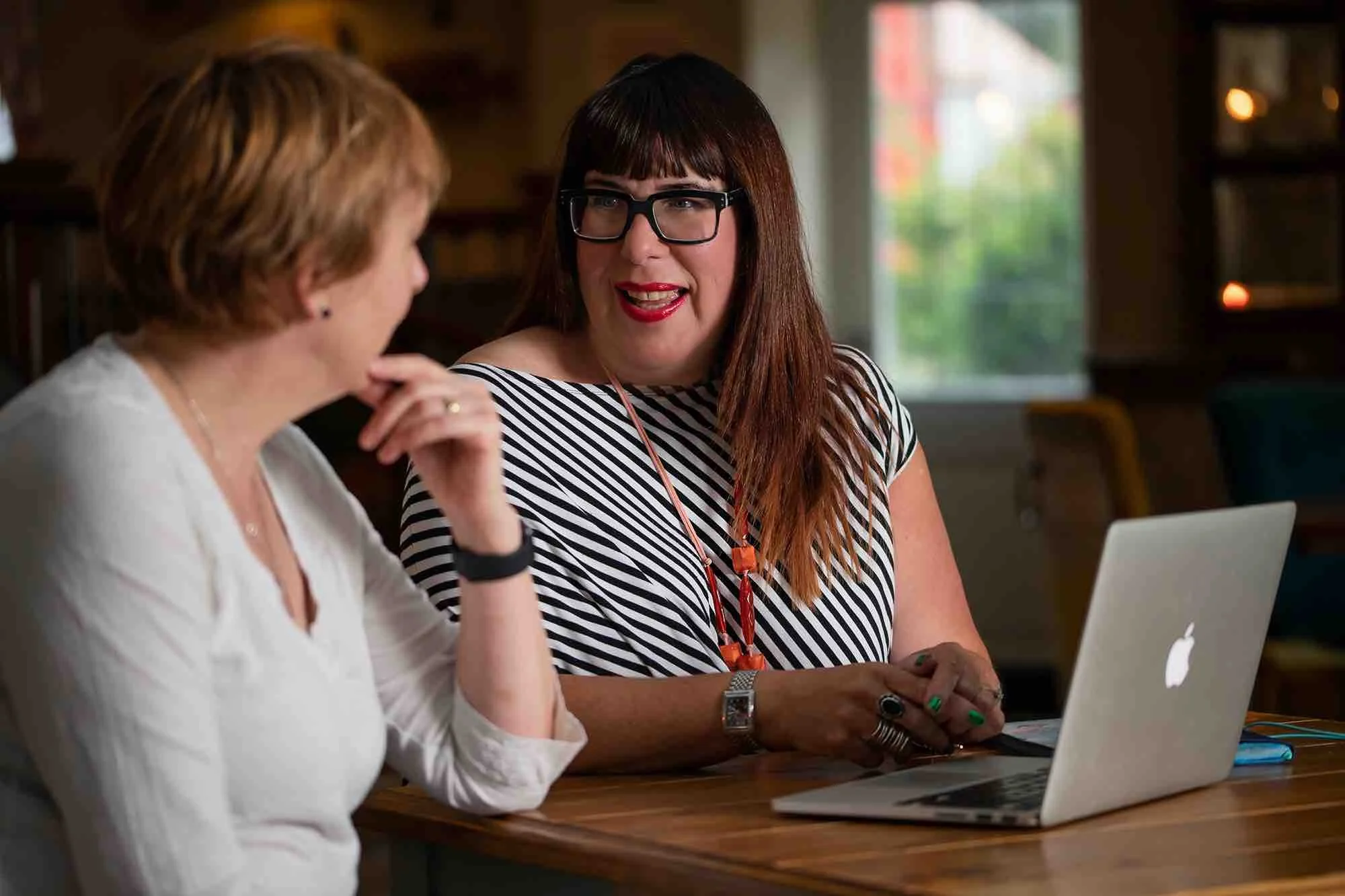 Two women having a conversation at a table with a laptop in a cozy, well-lit room.