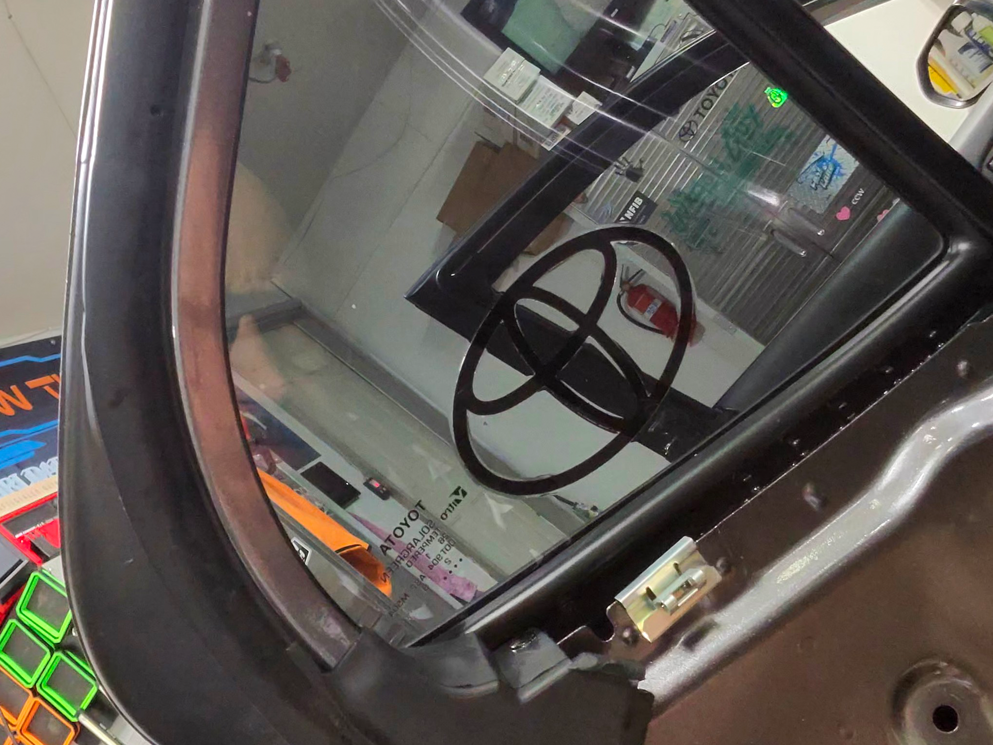 Close-up of a logo in window tint. shows a store interior with shelves, a fire extinguisher, and some signs.