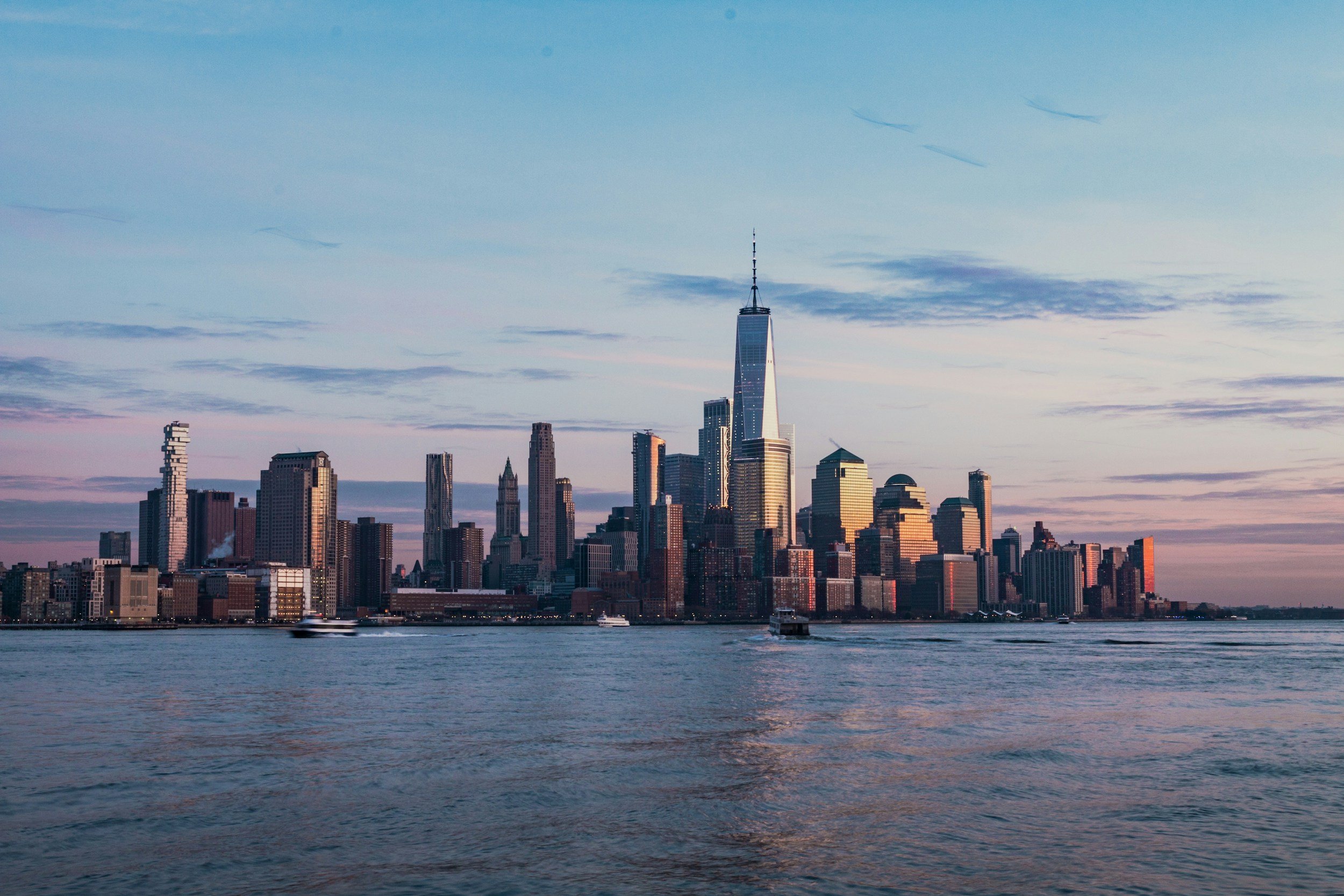 Skyline of New York City with One World Trade Center, viewed across the river during sunset.