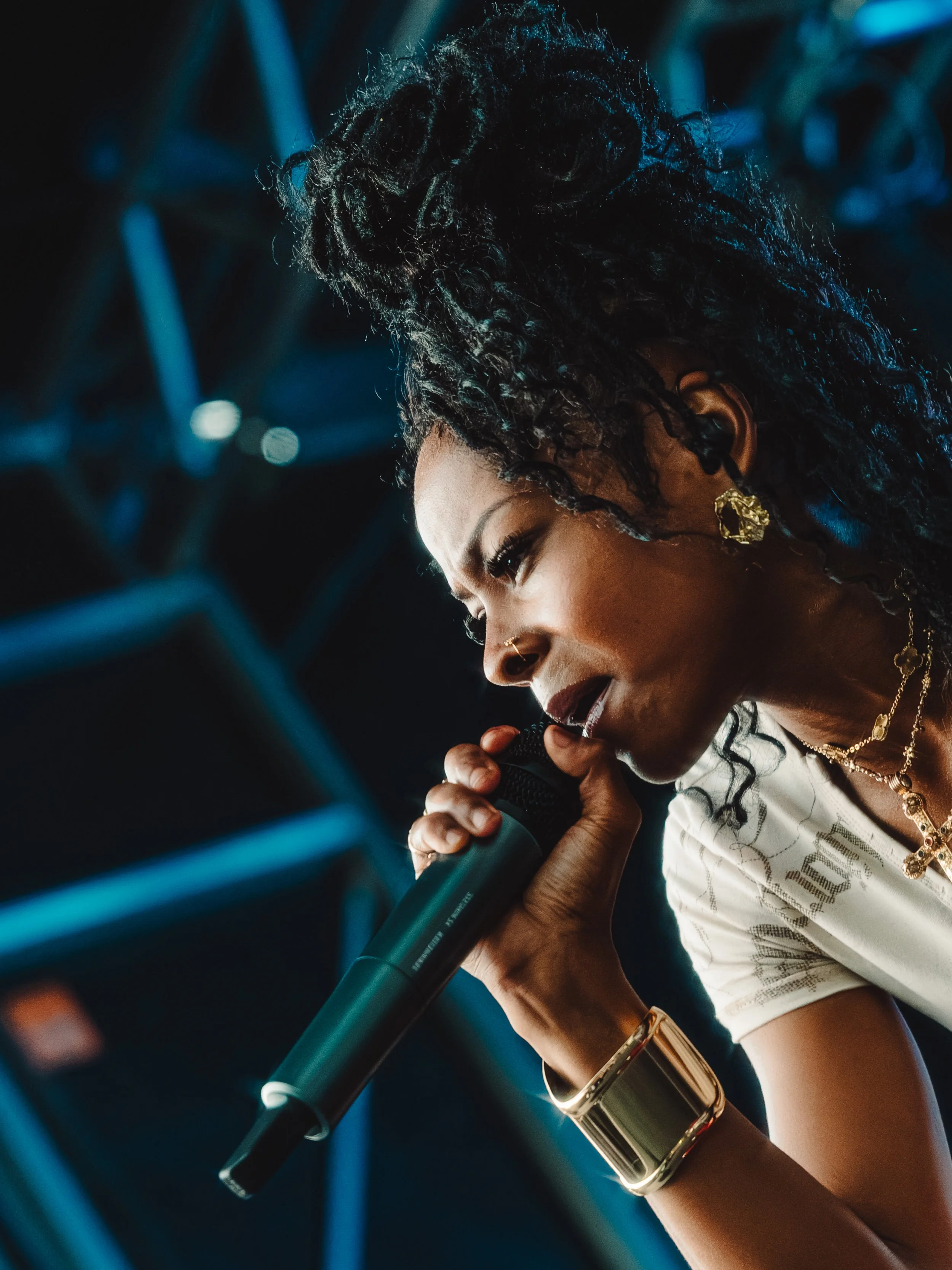A woman singing into a microphone on stage with a dark background and blue stage lights.