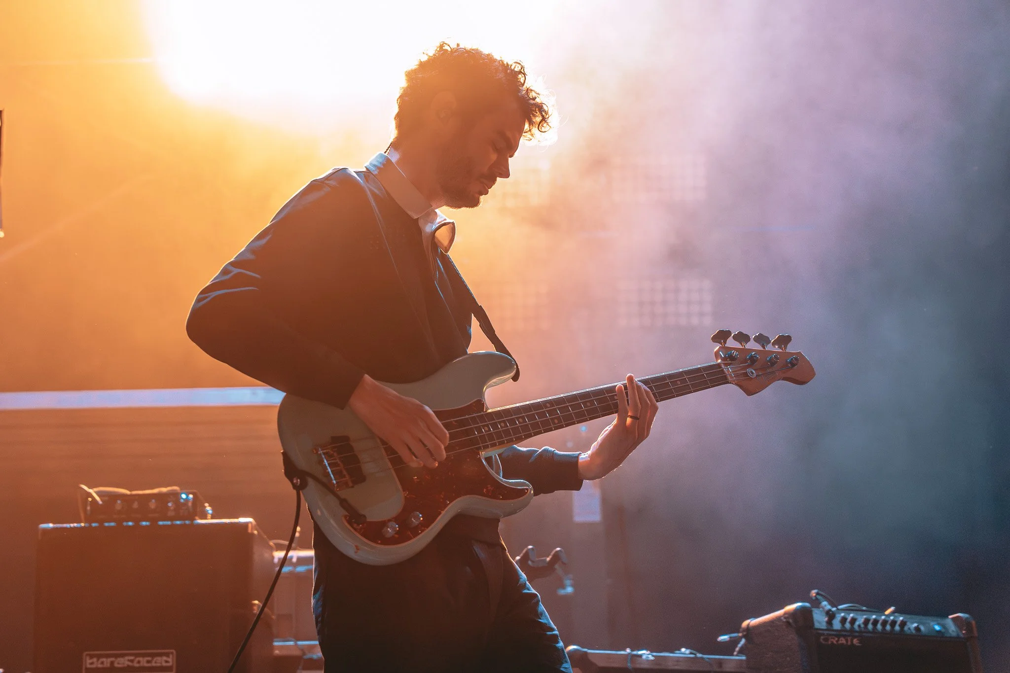 A male guitarist playing an electric guitar on stage, with bright stage lights and smoke around him.