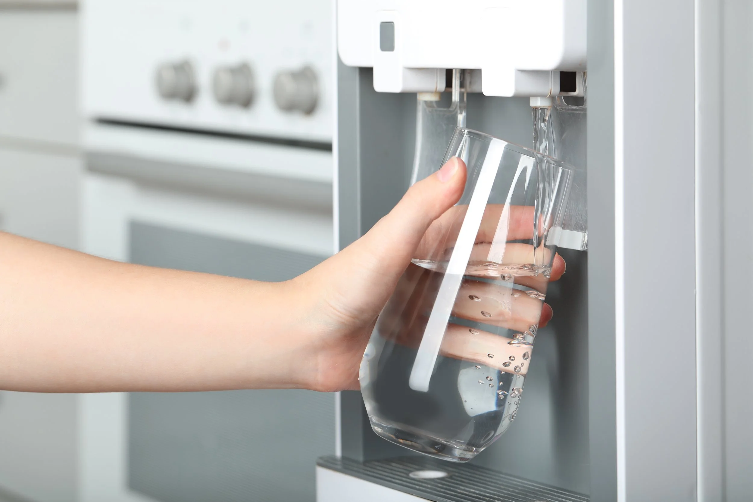 A person filling a glass with water from a water dispenser.