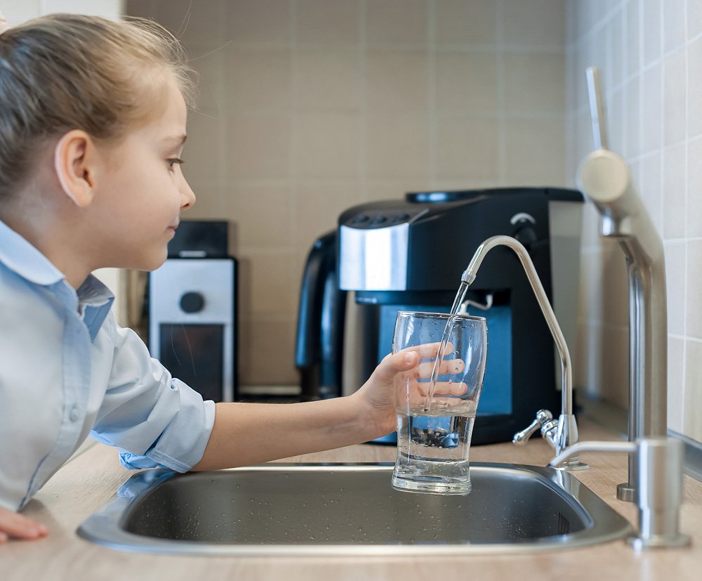 A girl filling a glass with water from a kitchen faucet.