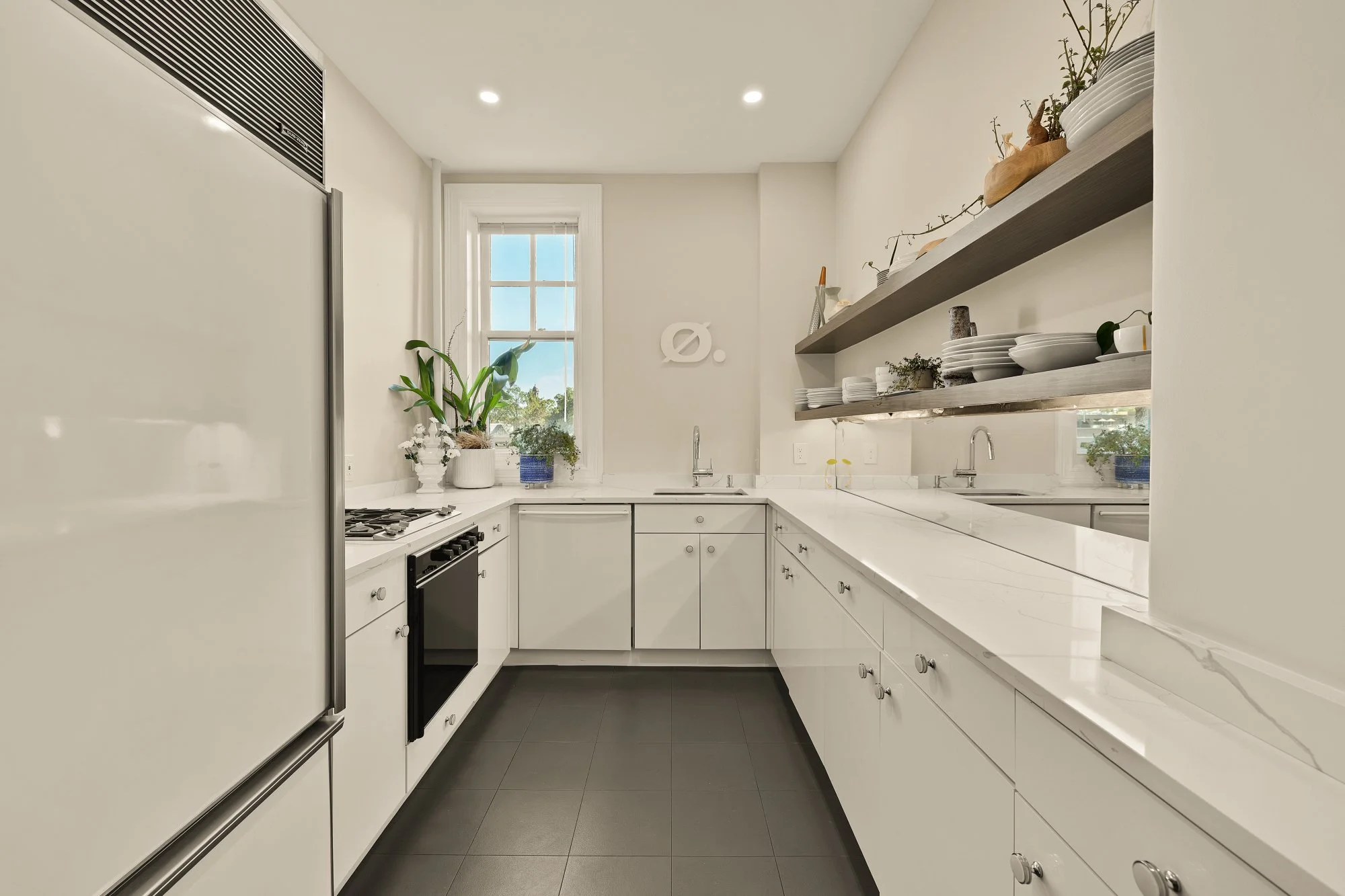 Bright modern kitchen with white cabinets, a black oven, a gas cooktop, a window with plants, and open shelves with dishes and decor.