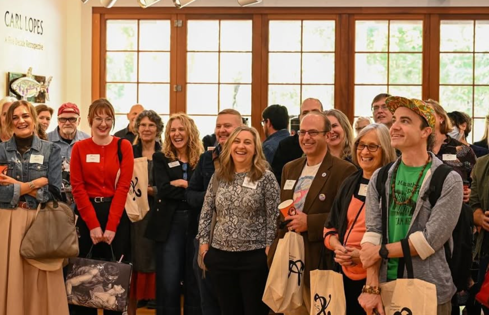 Group of people smiling and laughing at an indoor event, with large windows in the background.