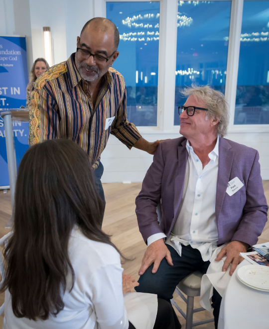 Arts Foundation of Cape Cod, Joe Digs 2025 Artist of the Year, Three people engaged in conversation at a professional event, two men and one woman, with a background of a modern indoor setting and a view outside the windows.
