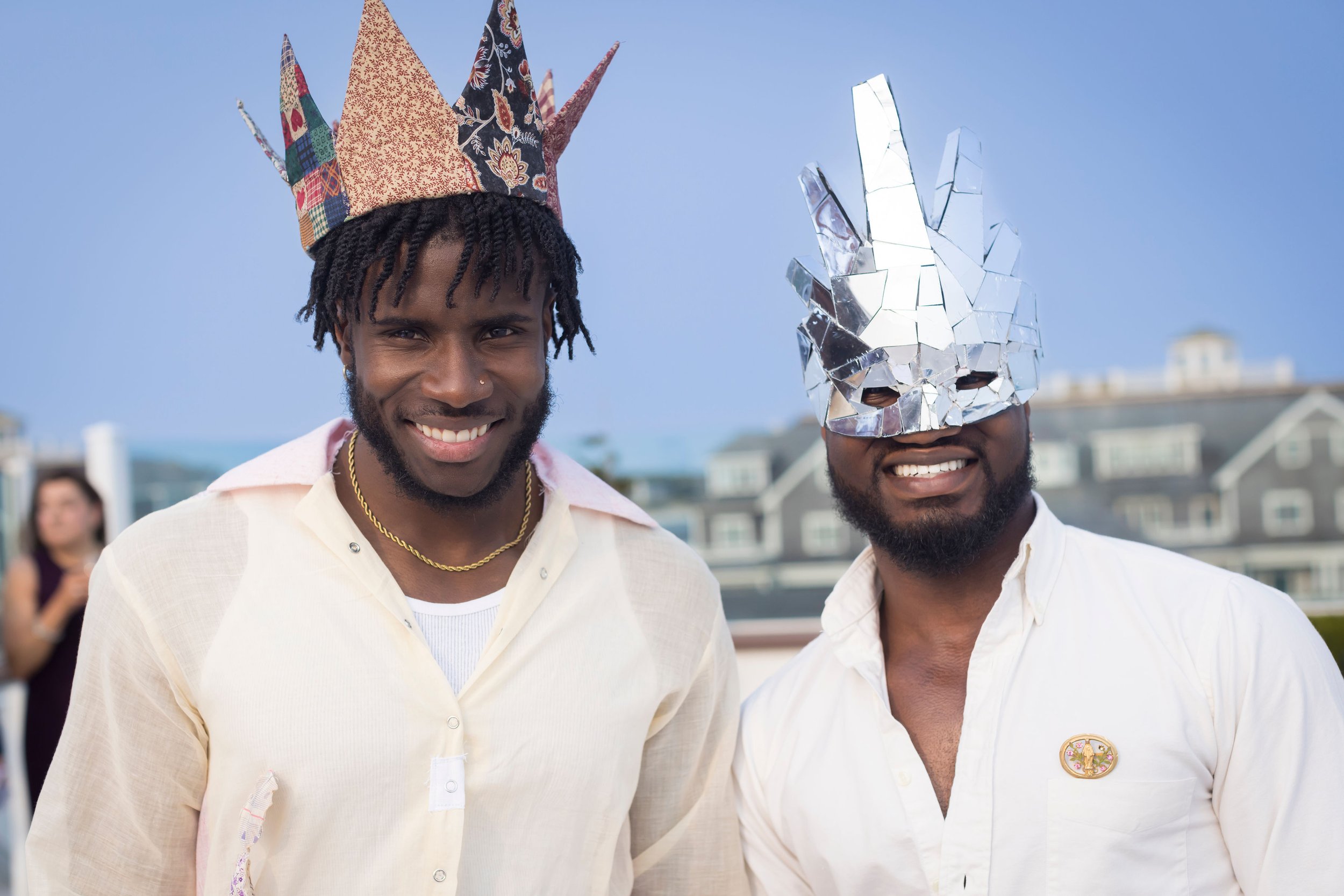 Arts Gala, Arts Foundation of Cape Cod, Two men smiling at an outdoor event, one wearing a colorful paper crown and the other wearing a reflective bunny mask, with a woman in the background.