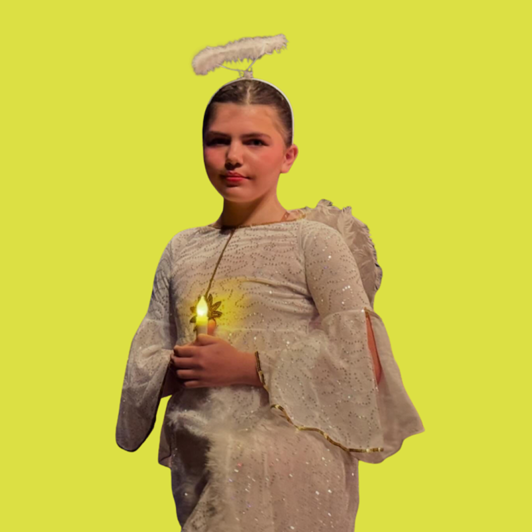 A young girl dressed as an angel, holding a glowing light in her hand, with a fluffy halo above her head, standing against a yellow background.