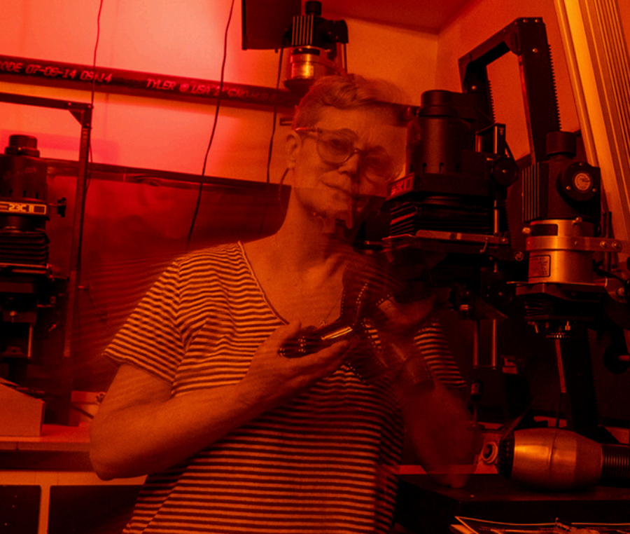 A woman in a striped shirt taking a selfie with a camera in a room with red lighting, scientific equipment, and machinery.