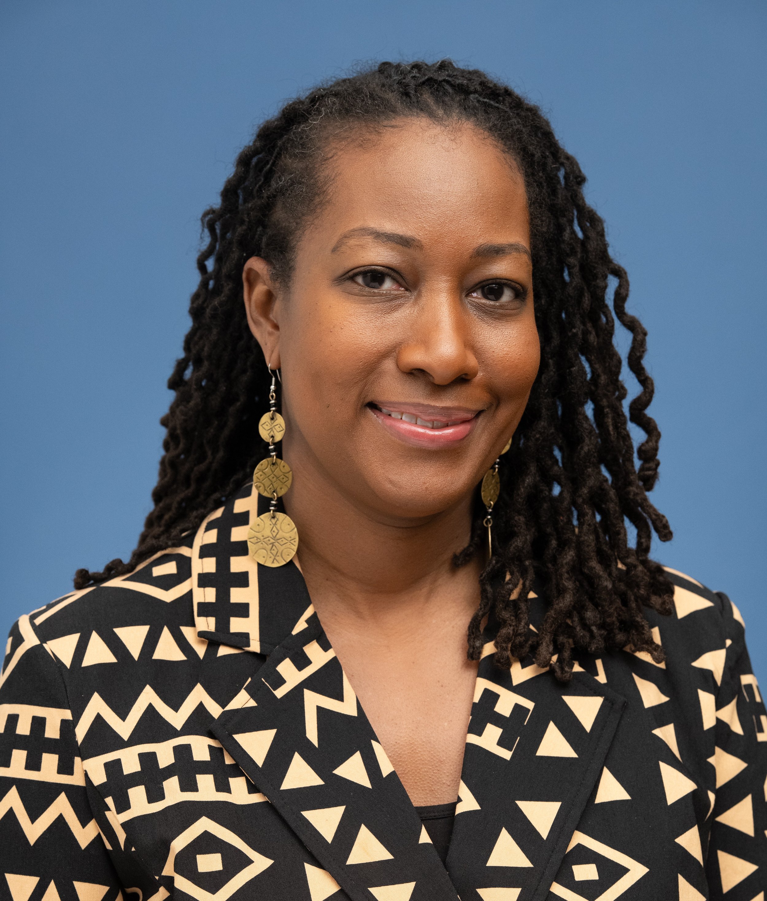 Photo of Dr. Abdullah wearing a black and tan blazer with long brass earrings