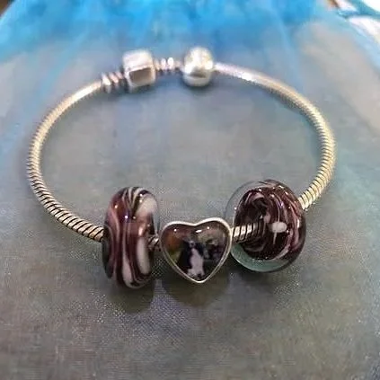 Silver bracelet with dark purple and marbled glass beads and a heart-shaped charm in the center.
