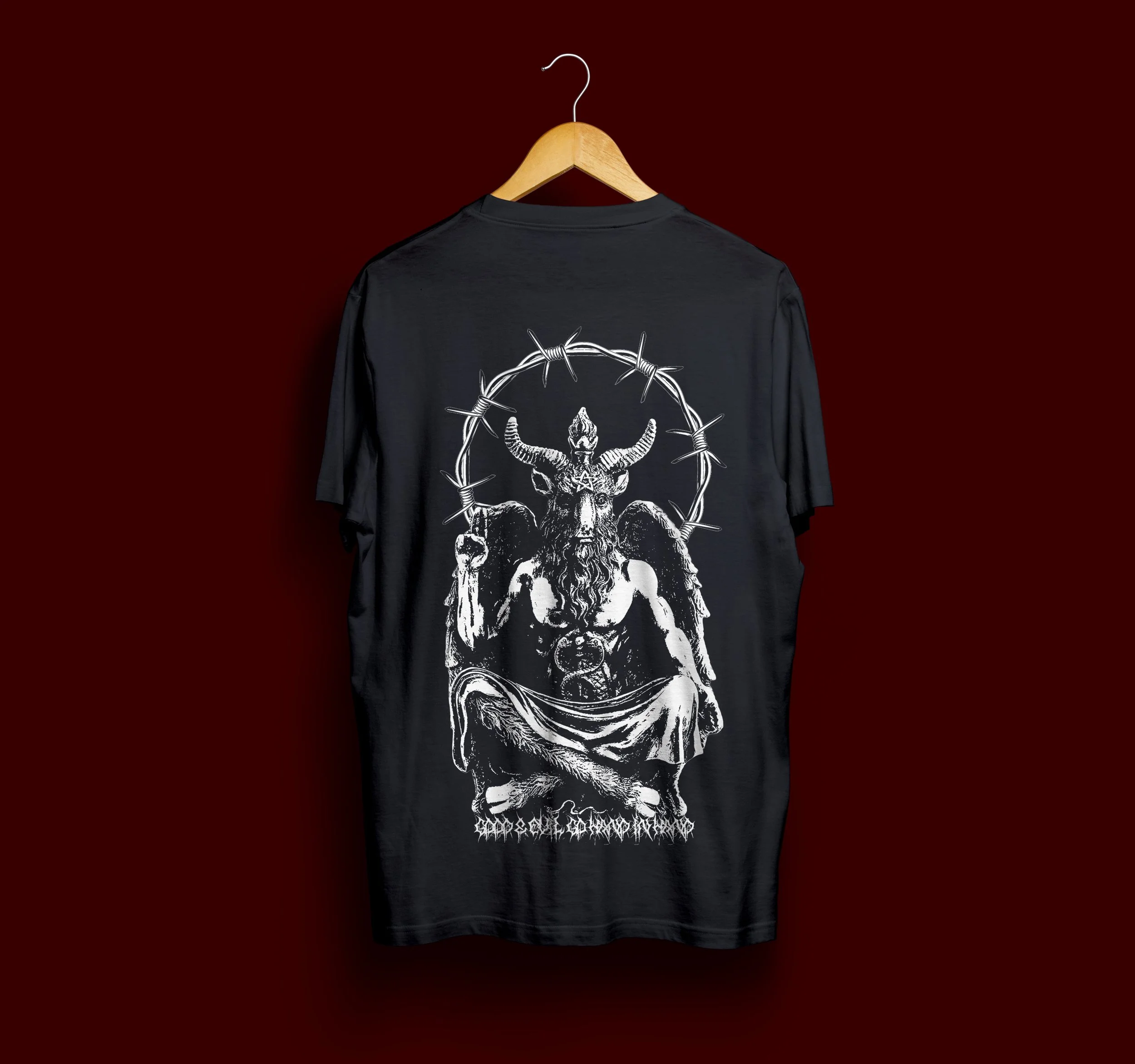 Black T-shirt featuring a white illustration of a mythological figure with a goat's head, horns, wings, and a raised fist, surrounded by barbed wire, against a dark red background.