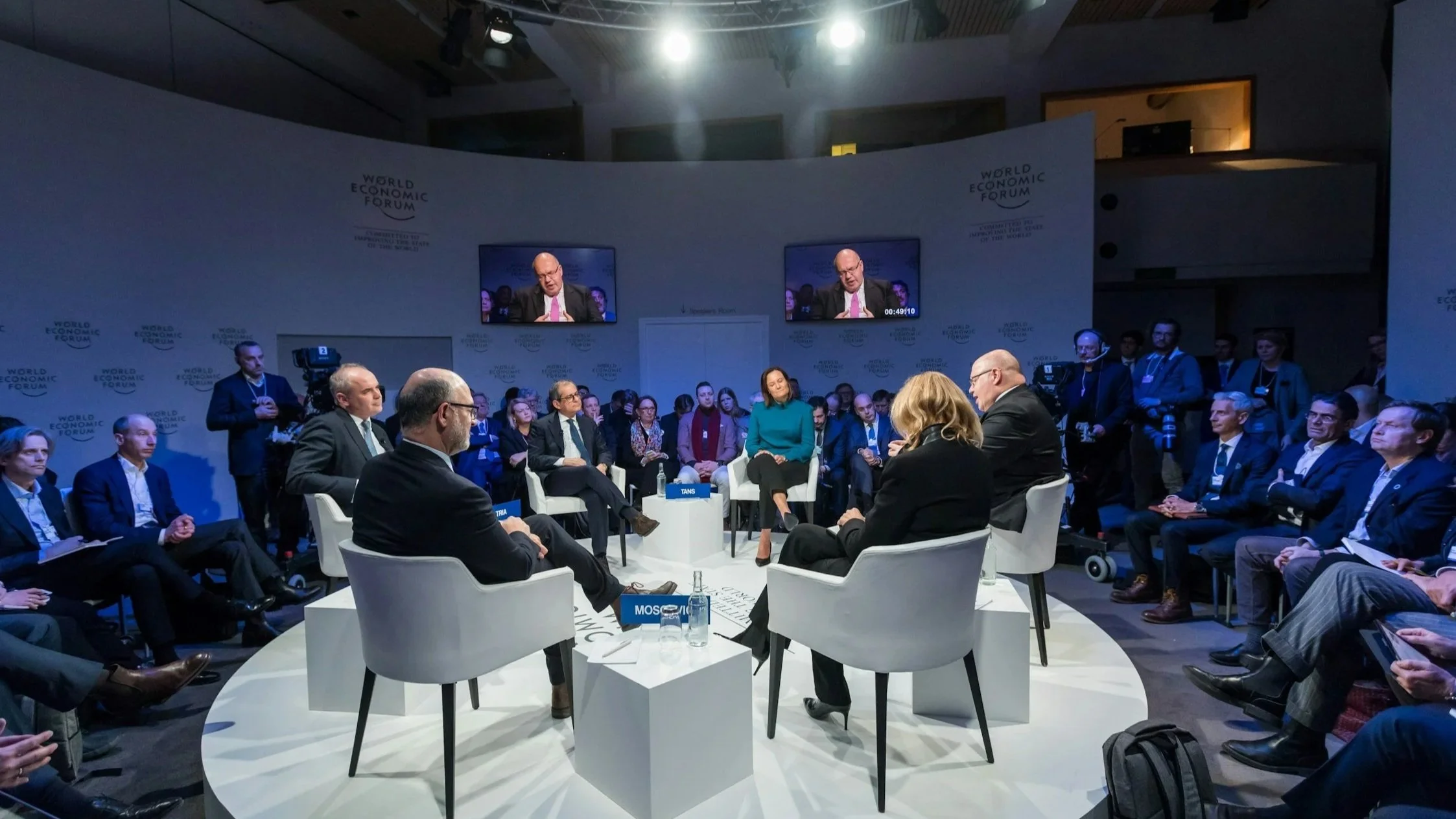 evento da industria da suplicy rsvp concierge. painel de discussão, com vários participantes sentado em roda e um público ao redor, incluindo telas no fundo exibindo um dos debatedores.