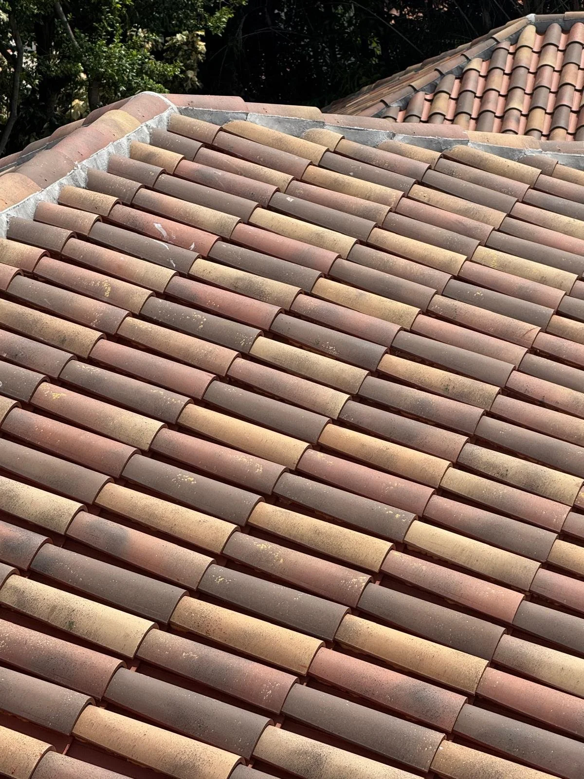 Close-up view of a tiled roof with curved, multicolored clay tiles in shades of pink, beige, and brown.