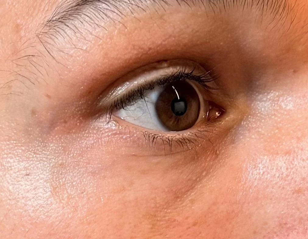 Close-up of a human eye with brown iris and surrounding skin.