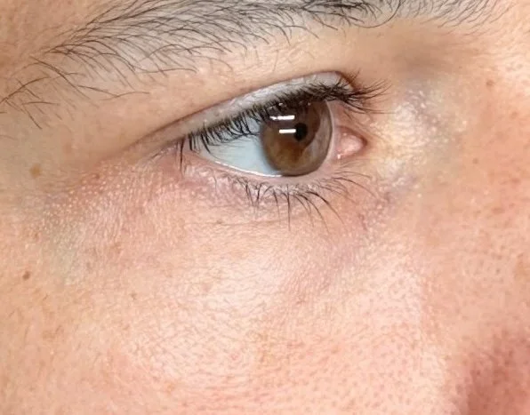 Close-up of a person's eye with brown iris and visible eyelashes.