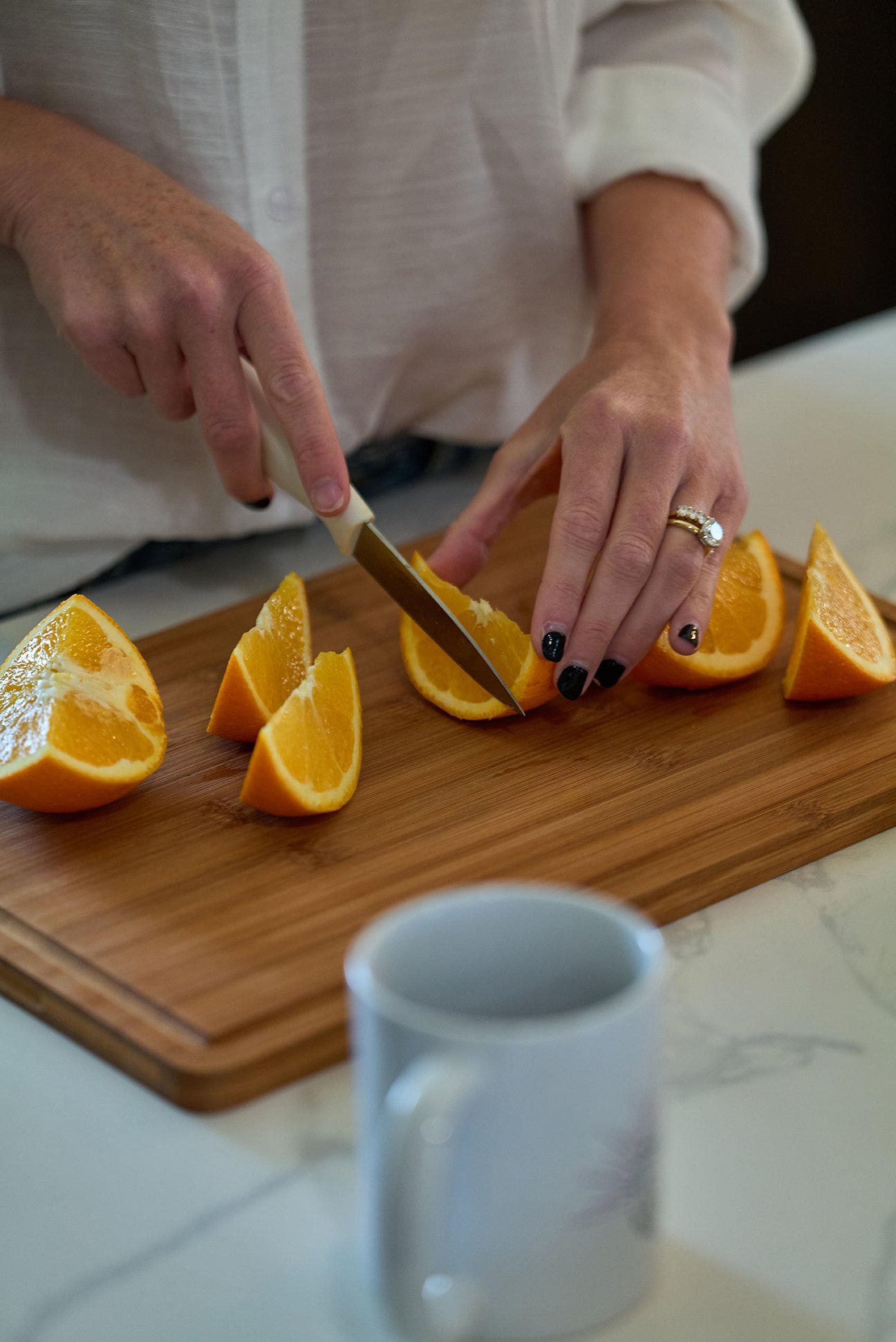 A person slicing oranges on a wooden cutting board.