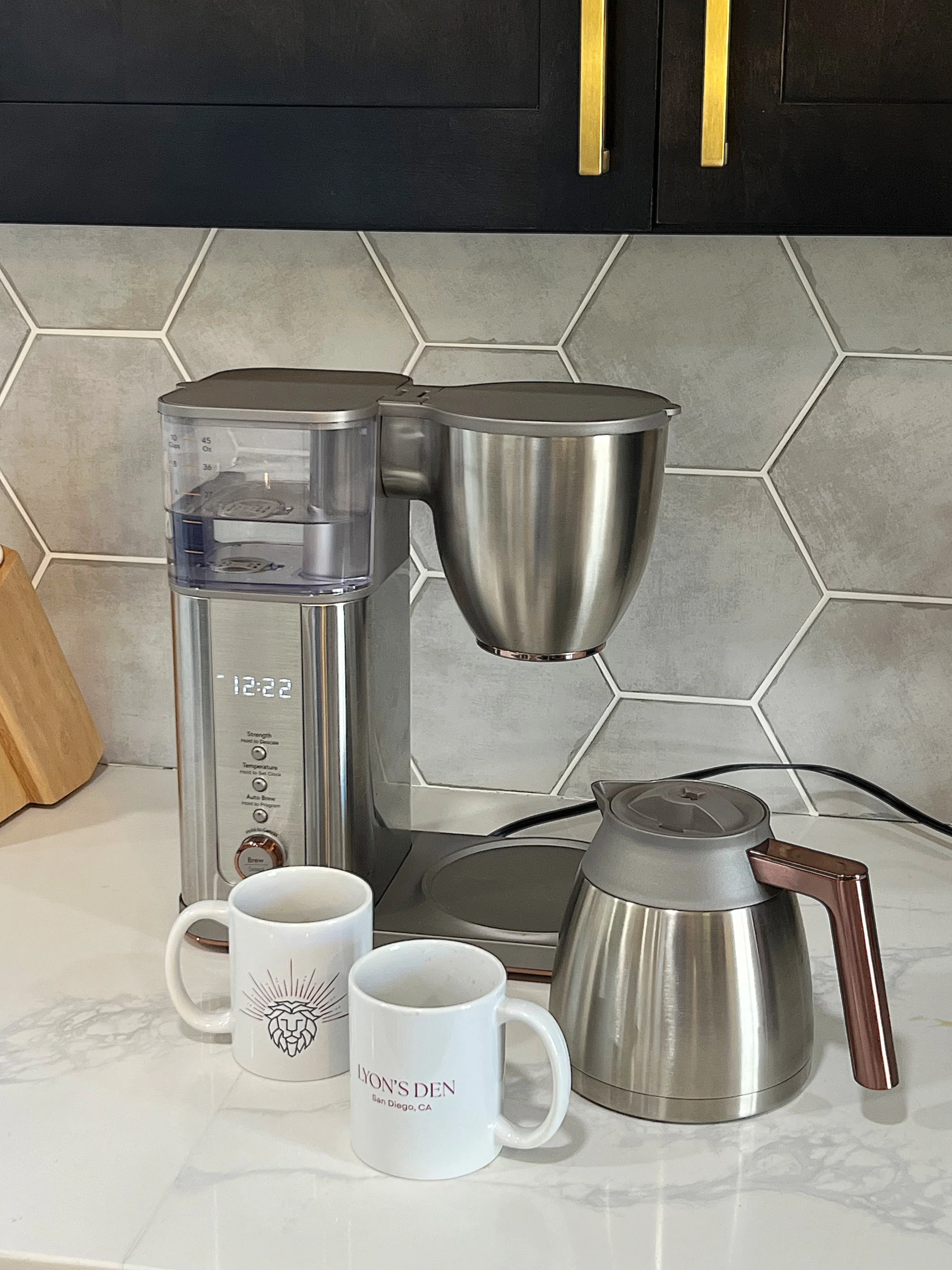 A modern kitchen countertop with an electric coffee maker, two white mugs, and a stainless steel electric kettle.