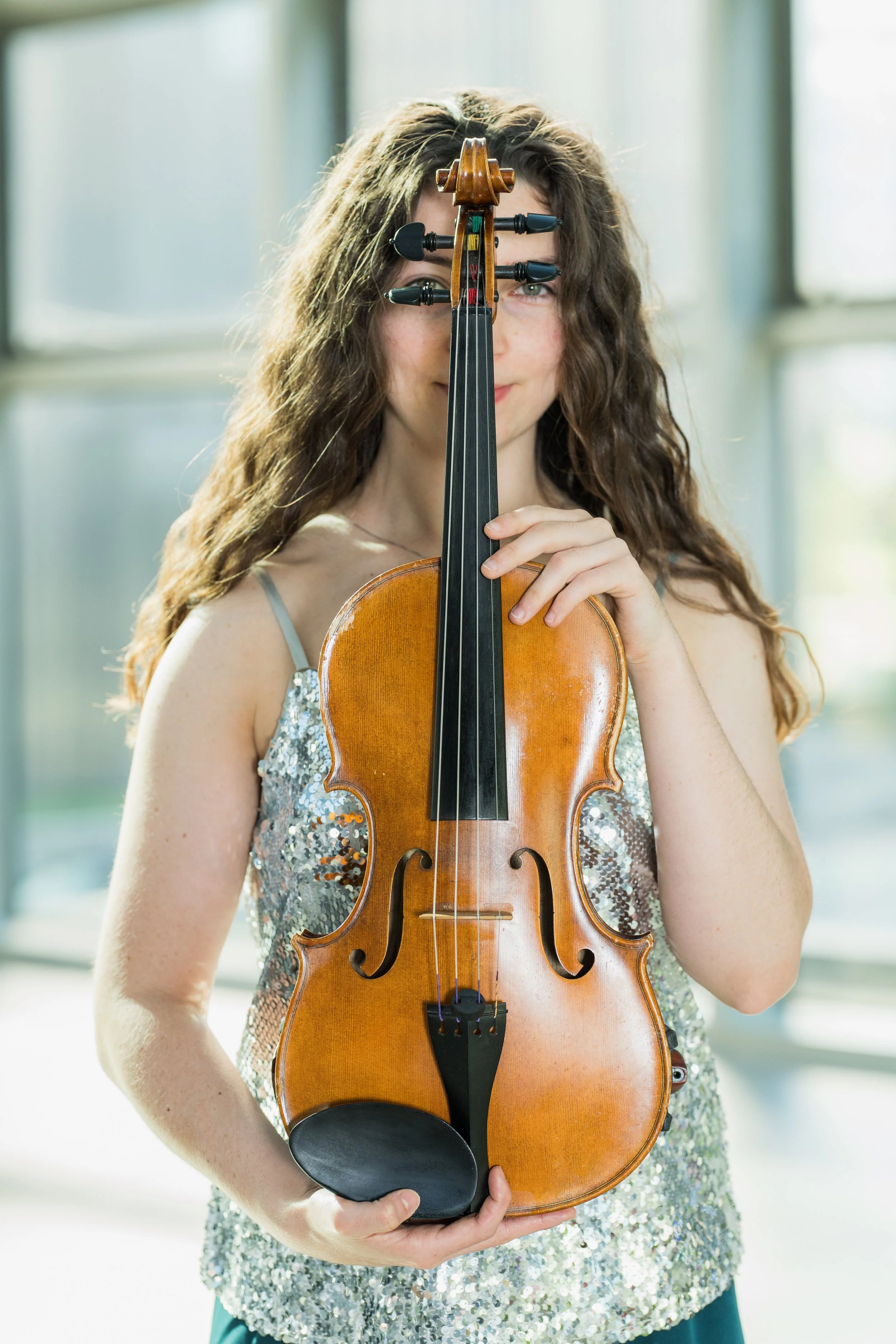 Erin Higgins holding a violin, standing indoors in front of a large window.
