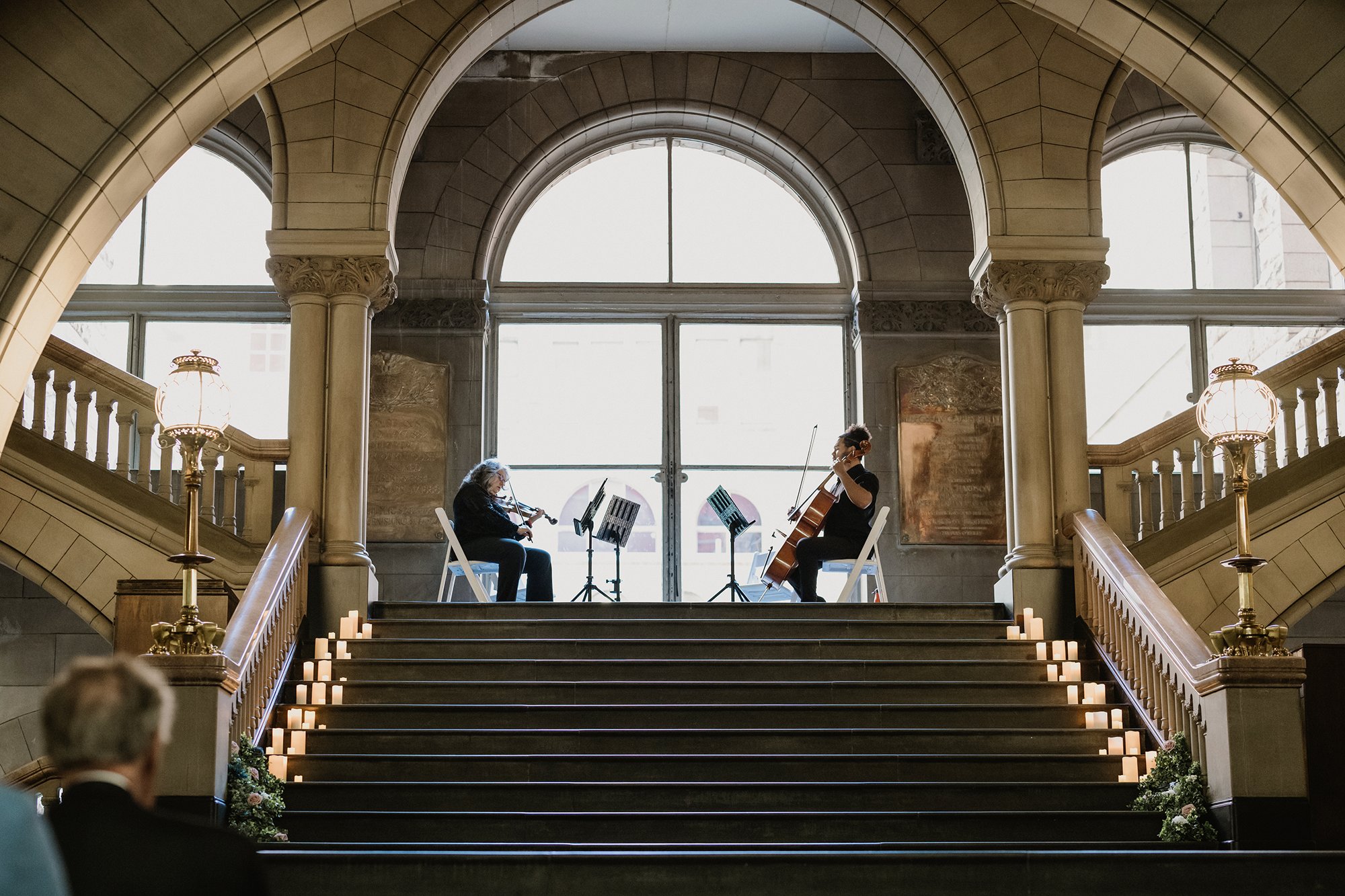 Radiant Strings playing violin and cello during a performance inside the Allegheny County Courthouse with large arched windows and candle decorations.