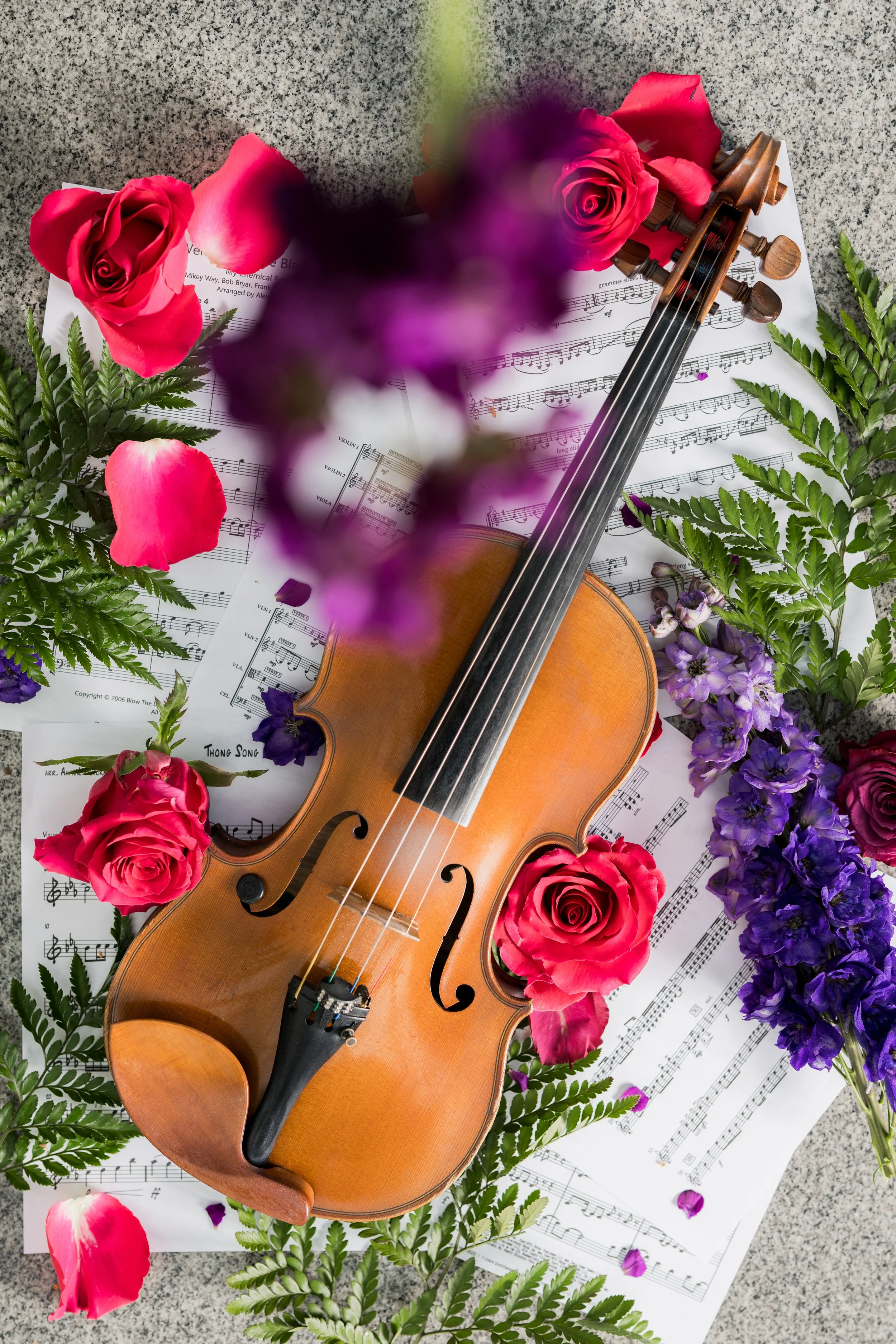 A violin surrounded by pink and purple flowers and sheet music.