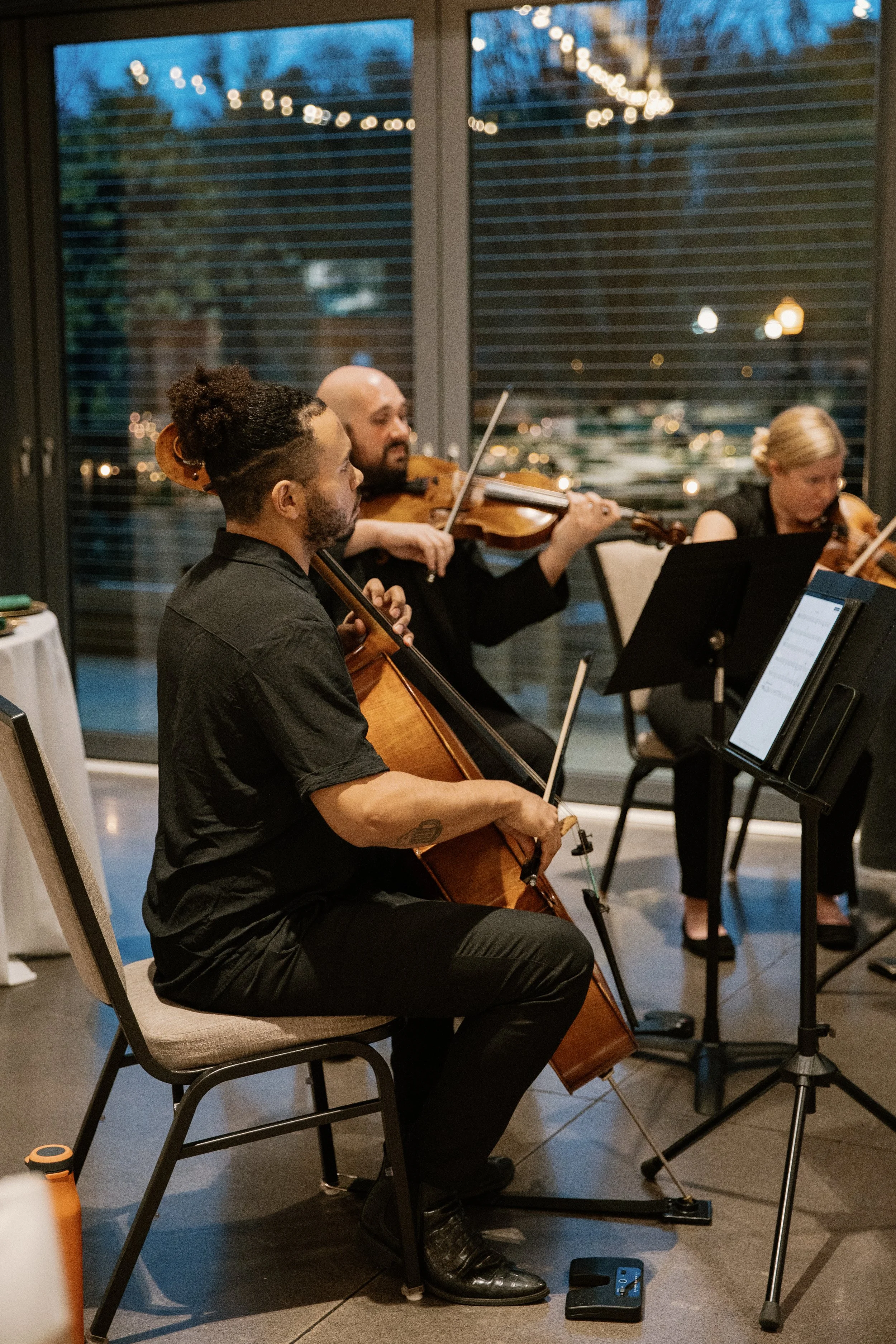 Radiant Strings playing at a performance indoors with large windows and string lights visible outside.