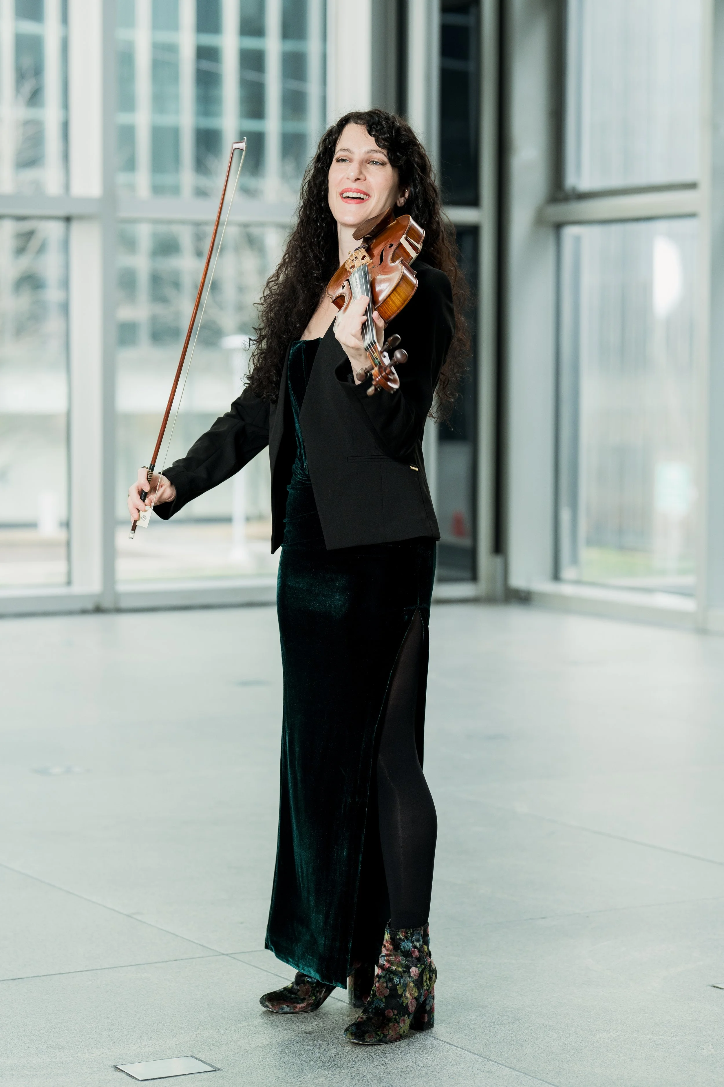 Cara Garofalo playing a violin inside a modern building with large glass windows.