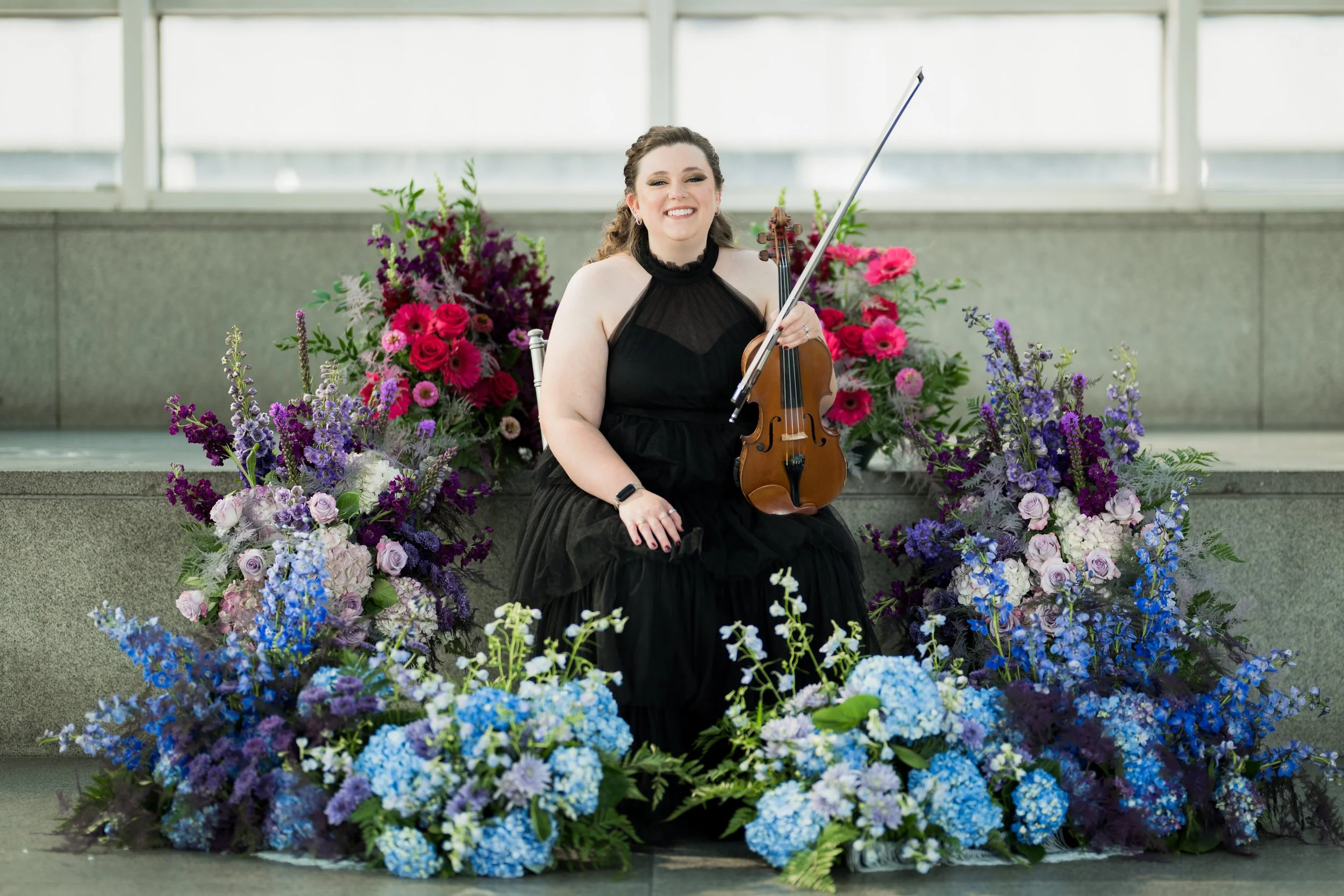 Nicole Lennartz holding her violin surrounded by flowers.