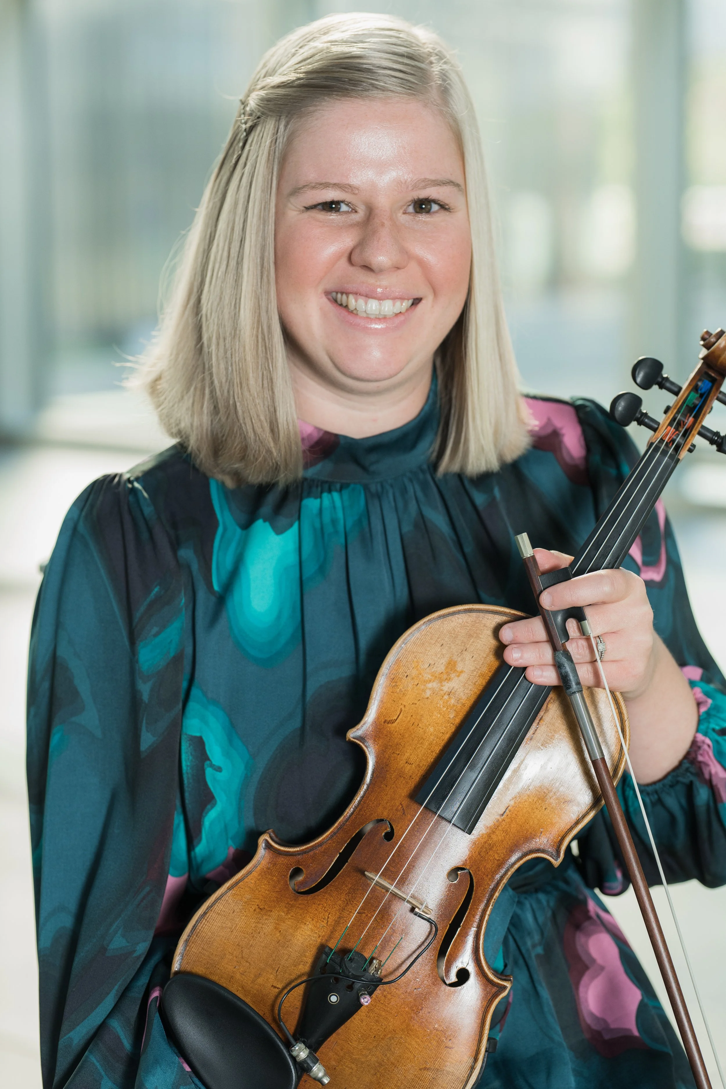 Amber Hooke smiles while holding a violin and bow.