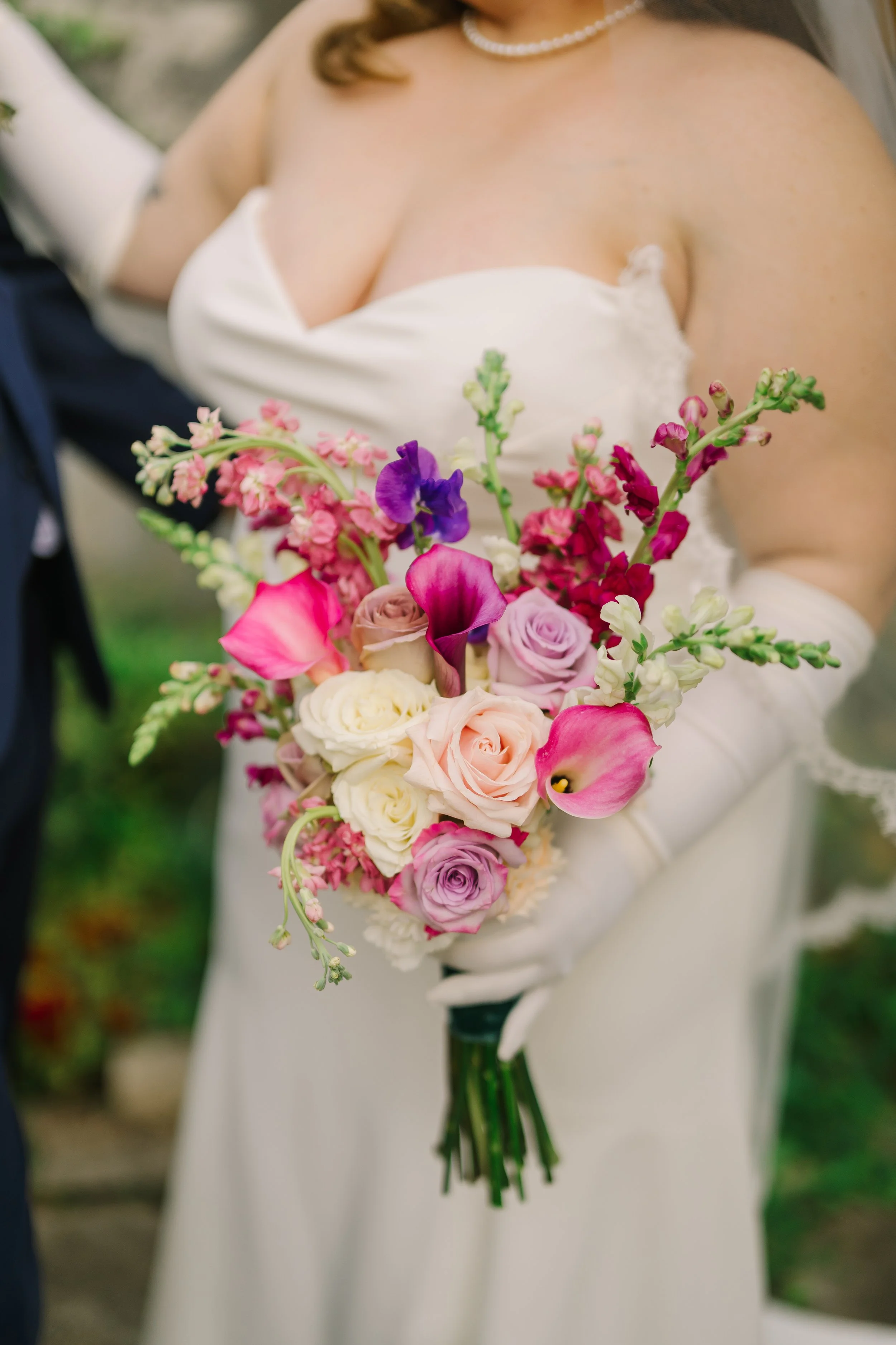 The bride dressed in her wedding gown holding a bouquet of pink, purple, and white roses and calla lilies.