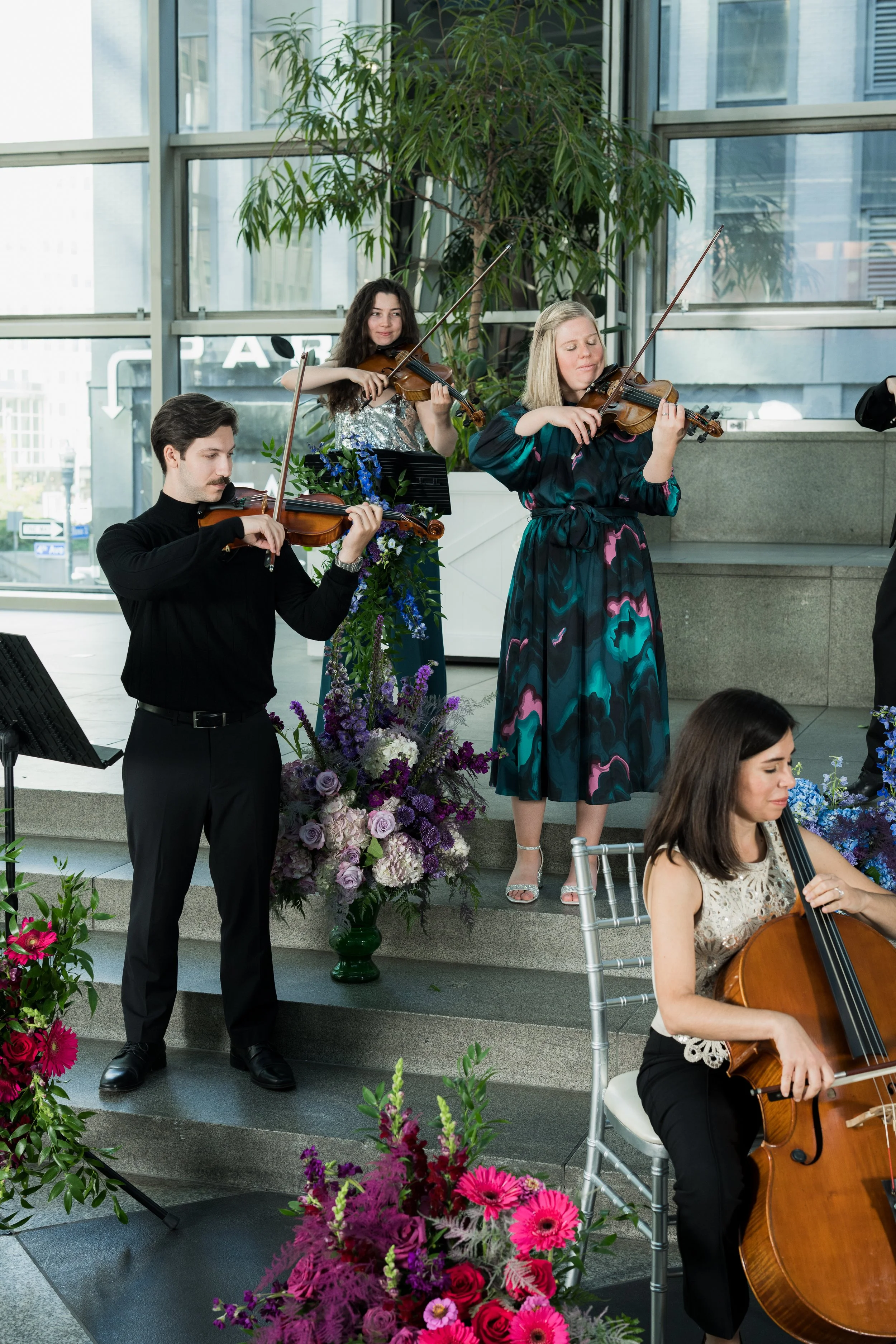 Anthony Cicco performing with Radiant Strings inside a modern building, surrounded by colorful flower arrangements.
