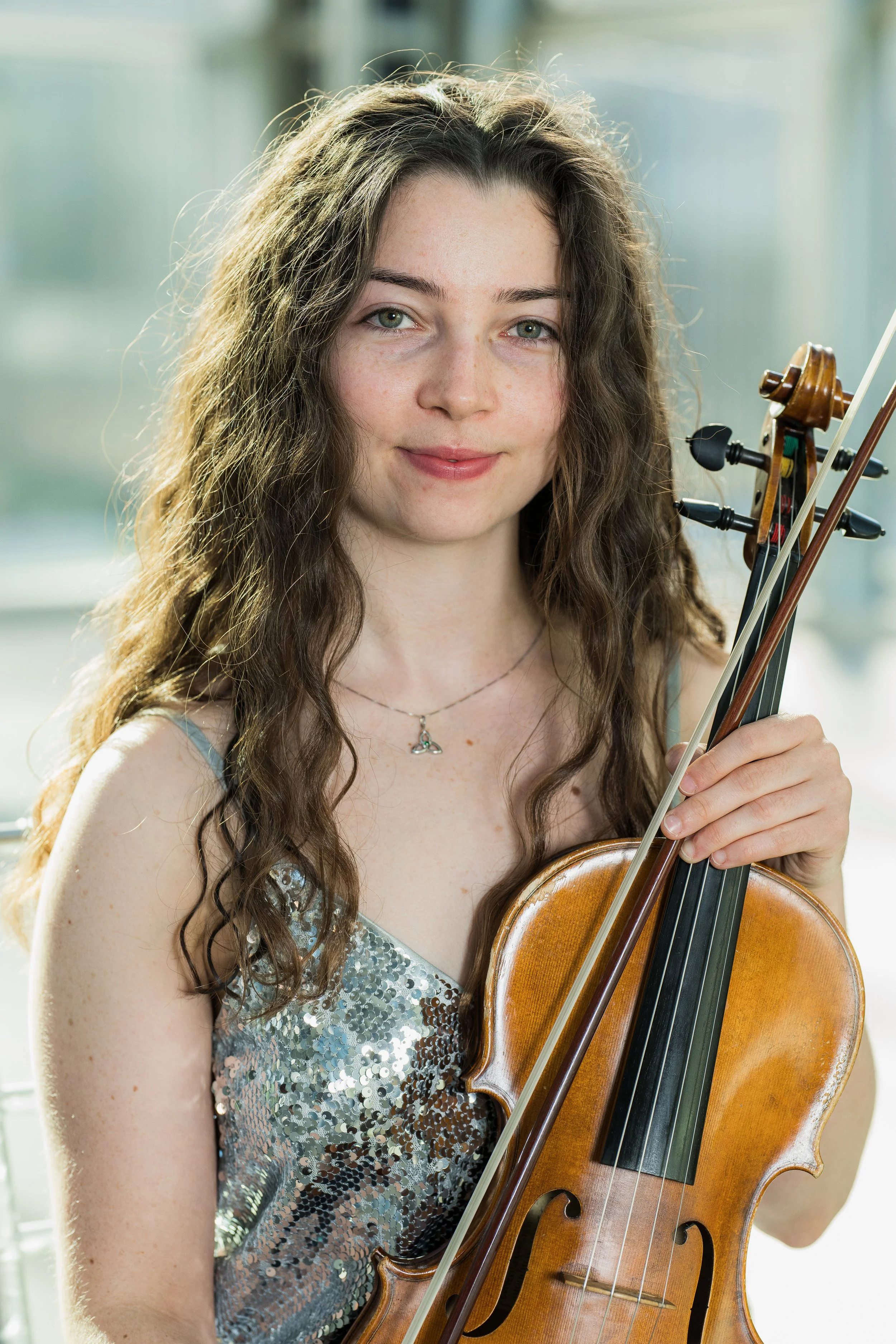 Erin Higgins holding a violin and bow, smiling, indoors with natural light.