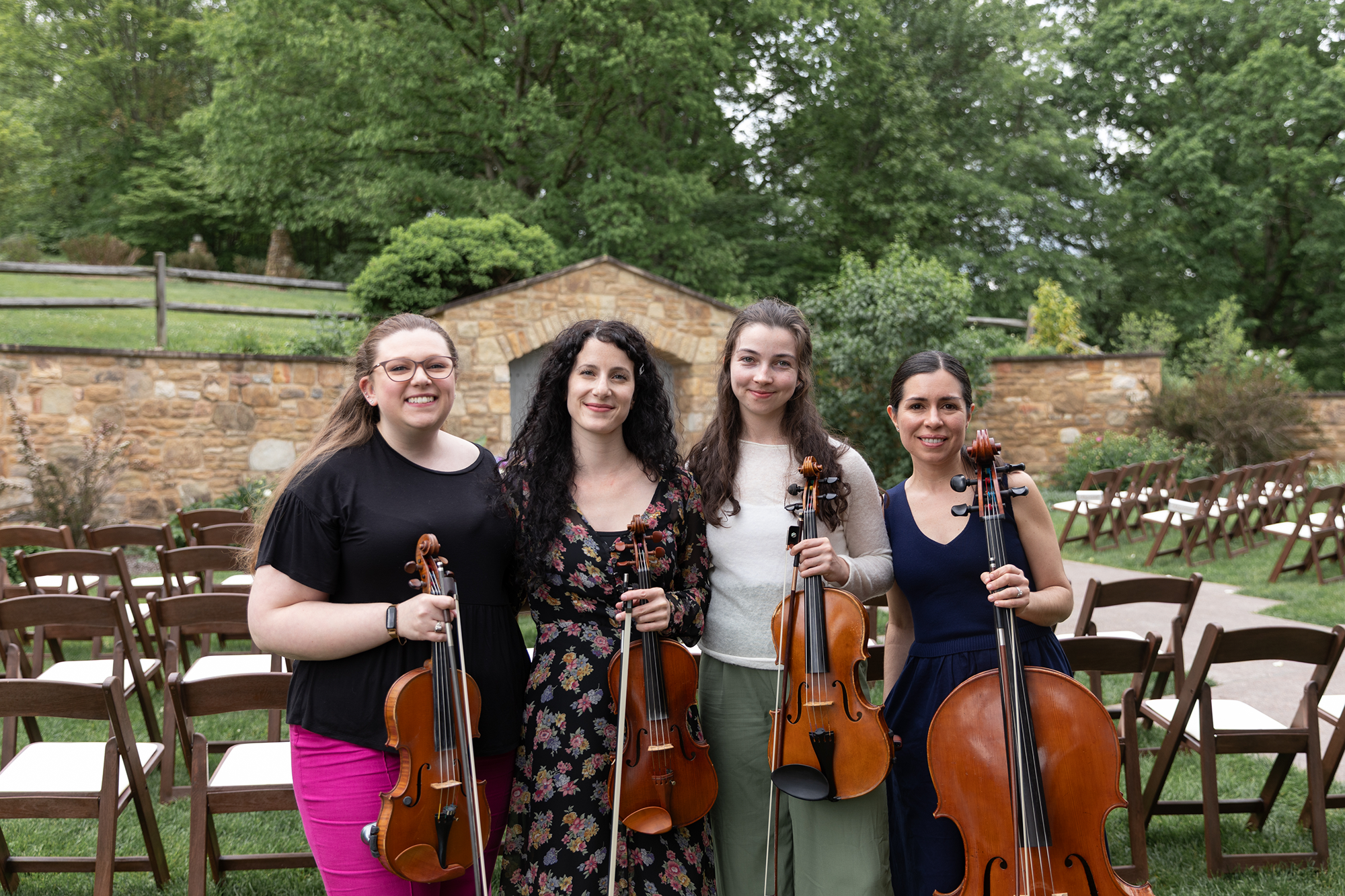 Radiant Strings standing in the Botanic Gardens each holding a string instrument, with chairs arranged behind them for a wedding ceremony.