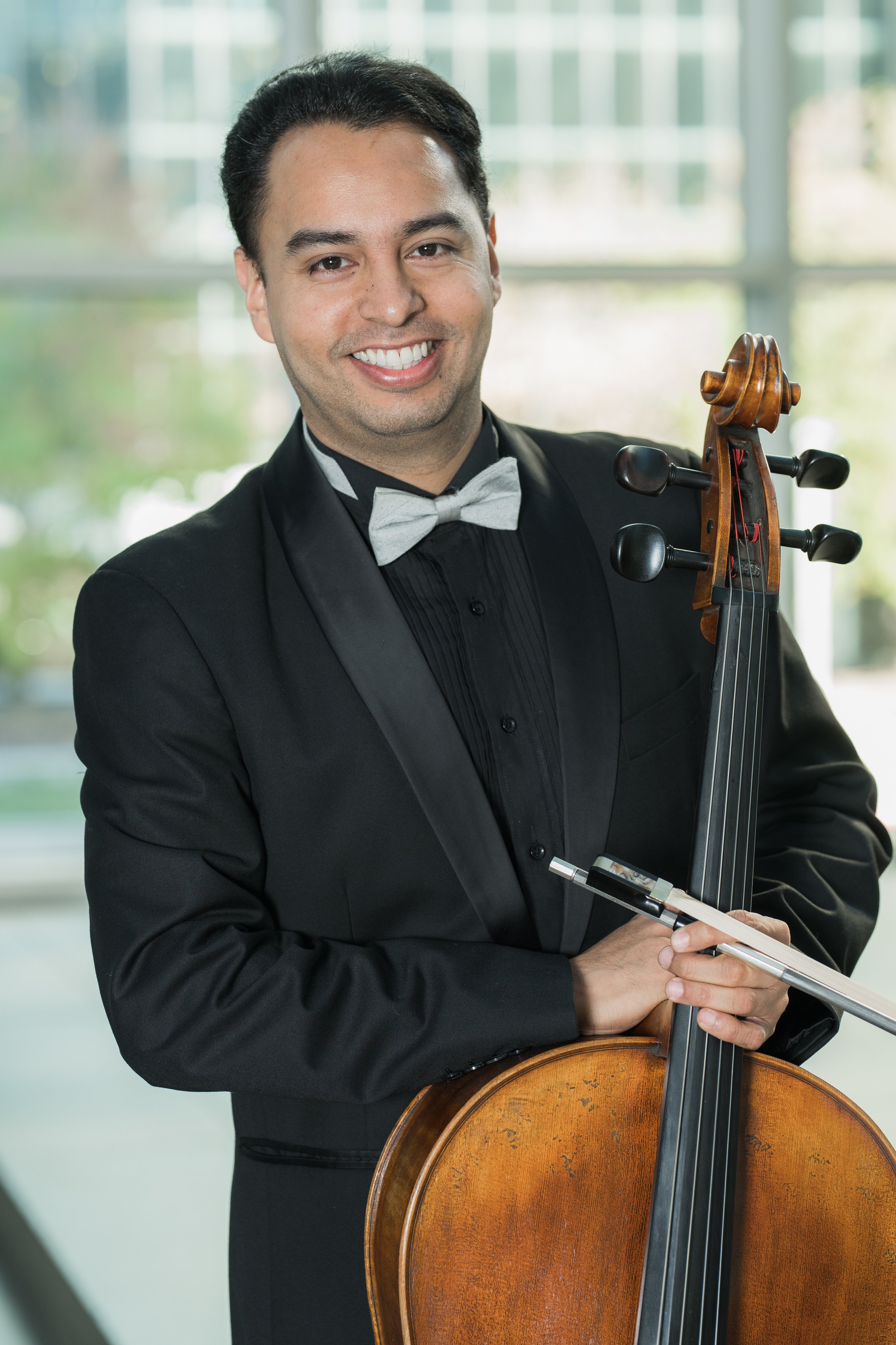 William Garcia smiling for a portrait with the scroll of his cello visible beside him.