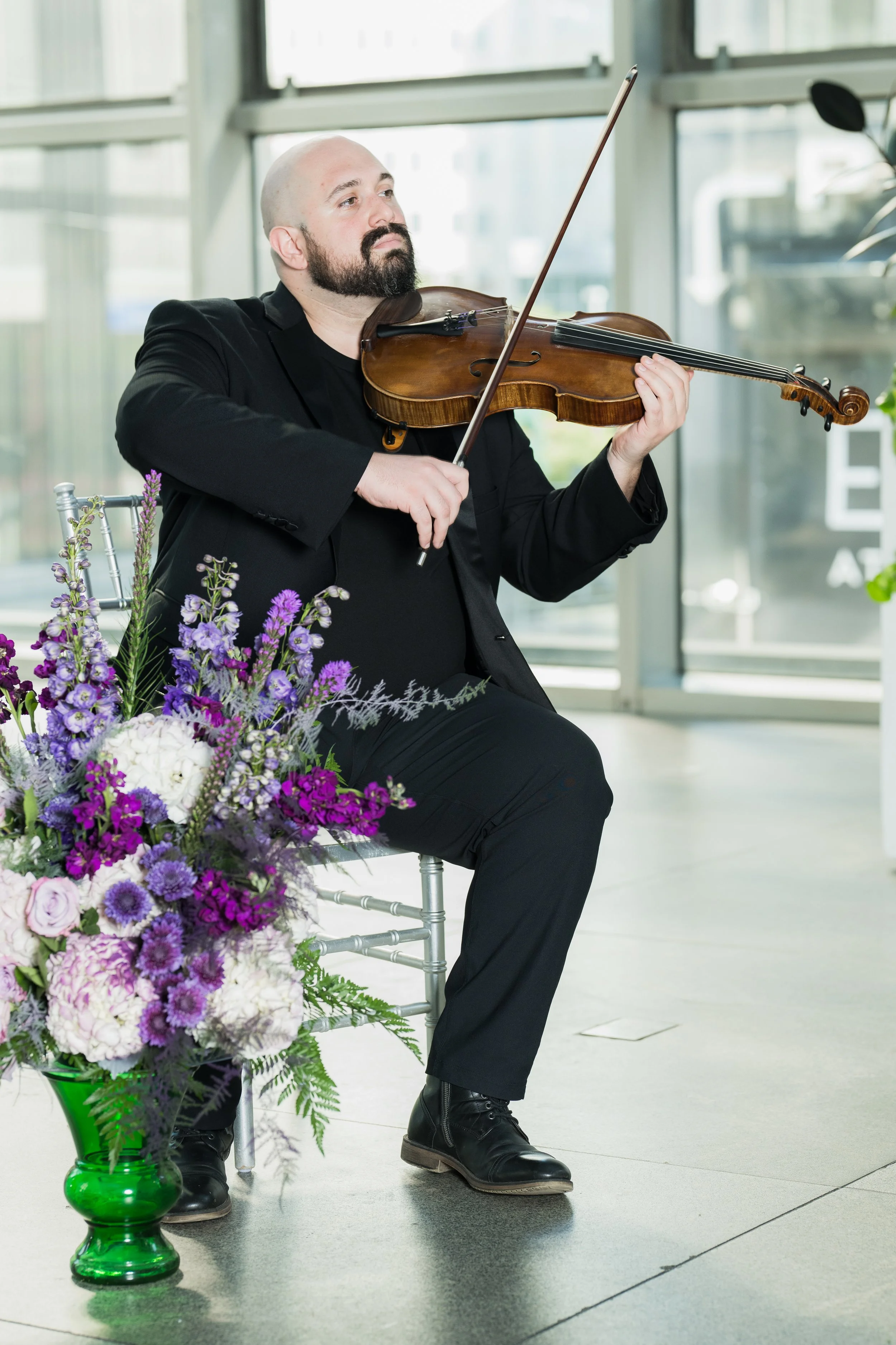 Stephen Weiss playing violin indoors next to flower arrangement.
