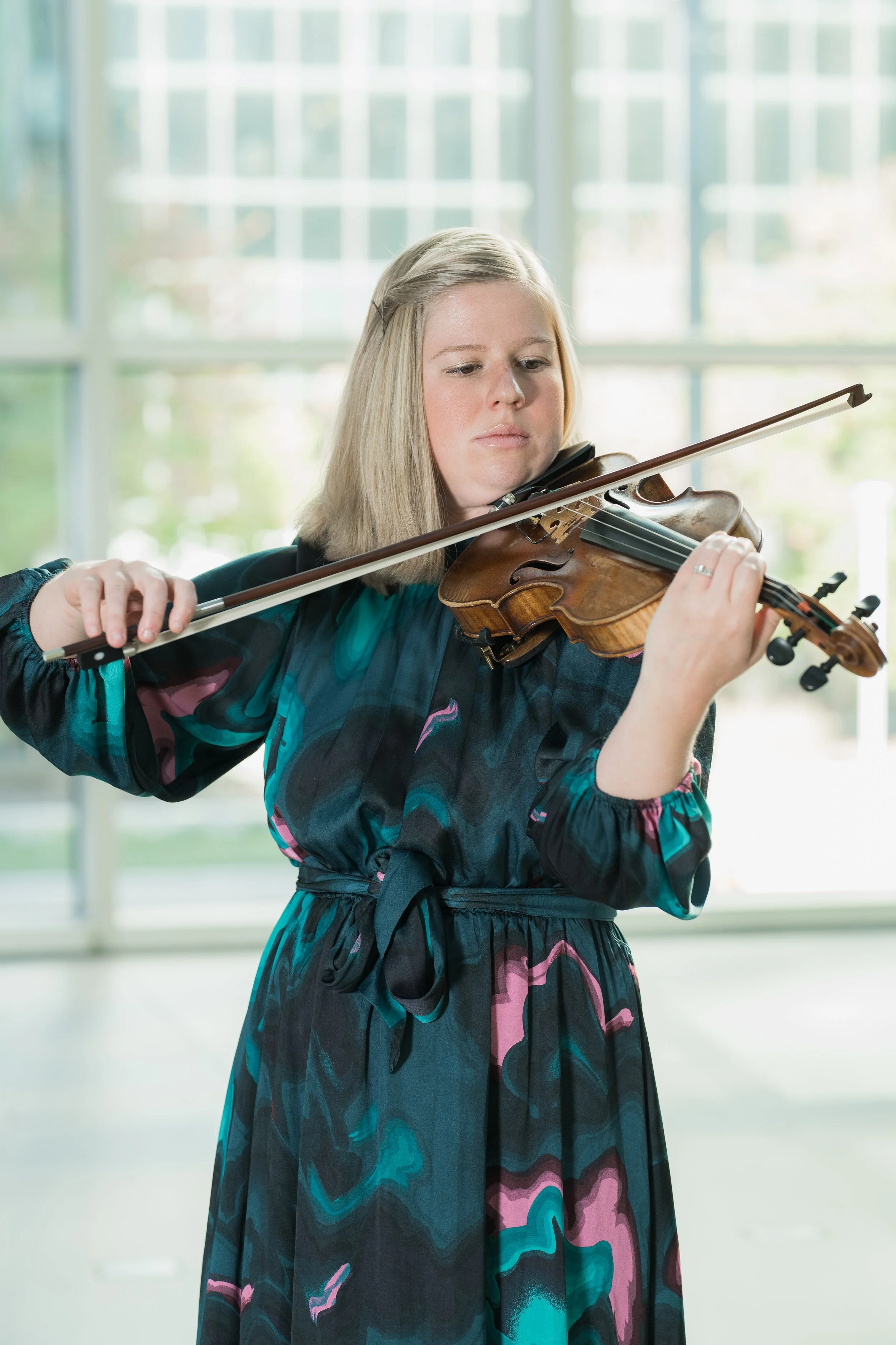 Amber Hooke playing the violin indoors near large windows.